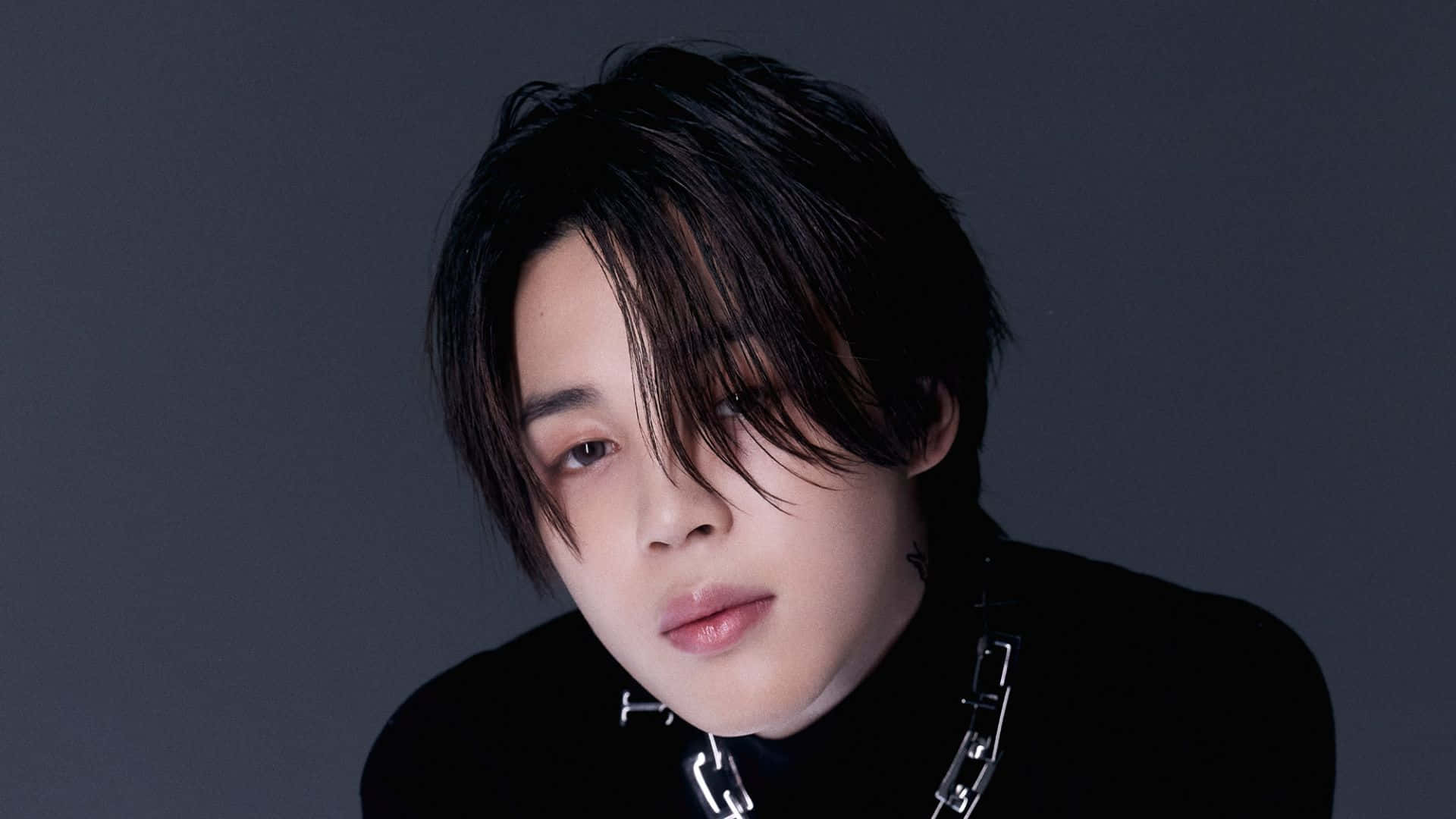 深色頭髮、戴著鏈條項鍊的年輕男子溫柔地看著鏡頭。 — Jimin GIF 壁紙