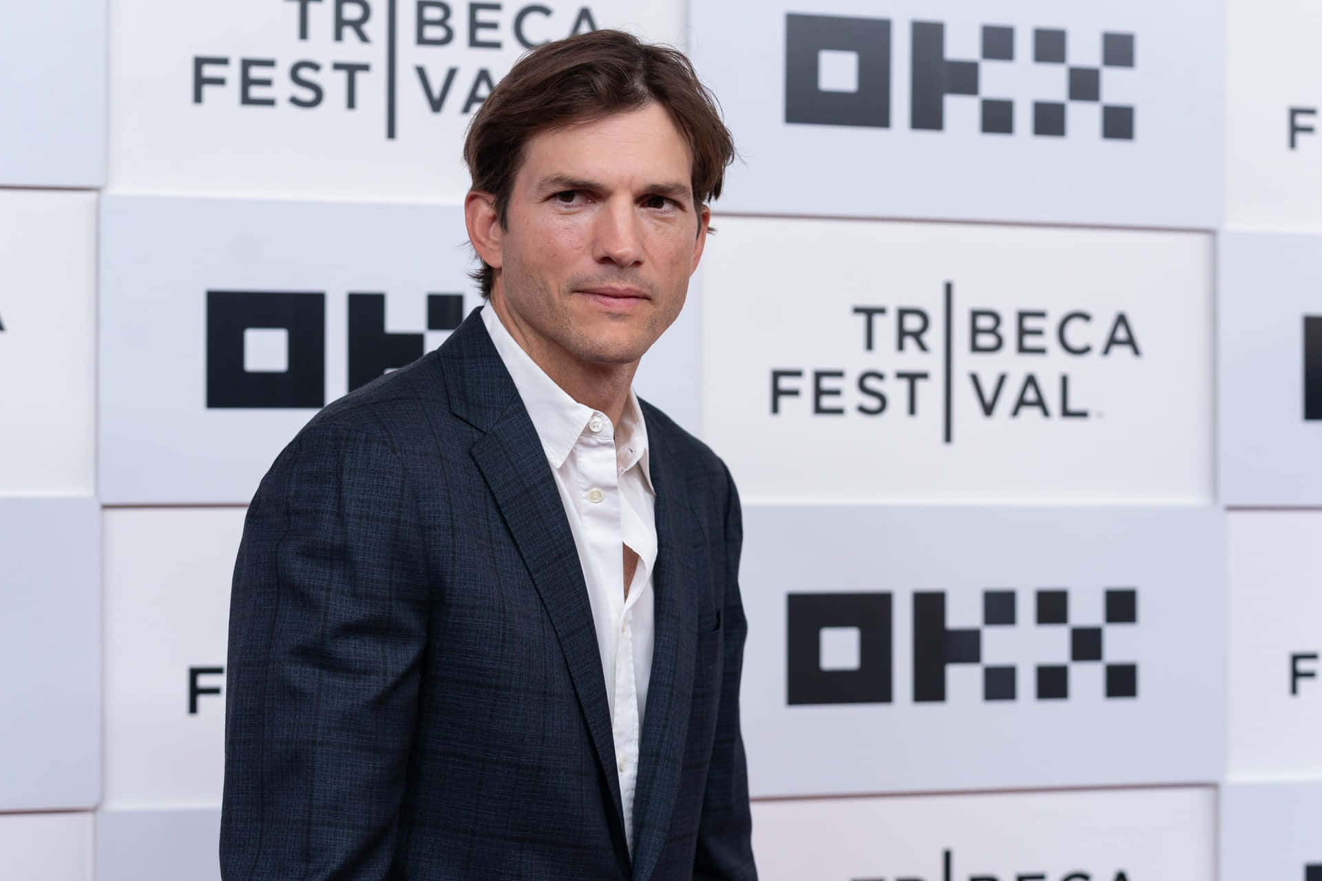 演員艾斯頓·古查在Tribeca Festival穿著深色西裝和白色襯衫。