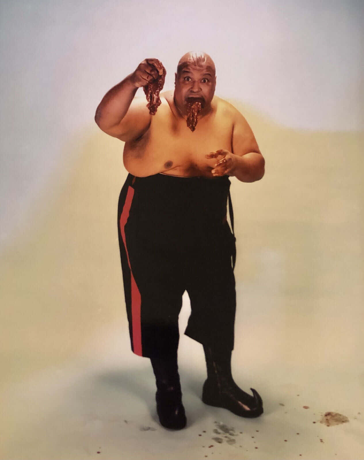 一個穿著帶有紅色條紋黑色褲子的男人正在吃肉，醬汁從他的嘴裡滴下來。