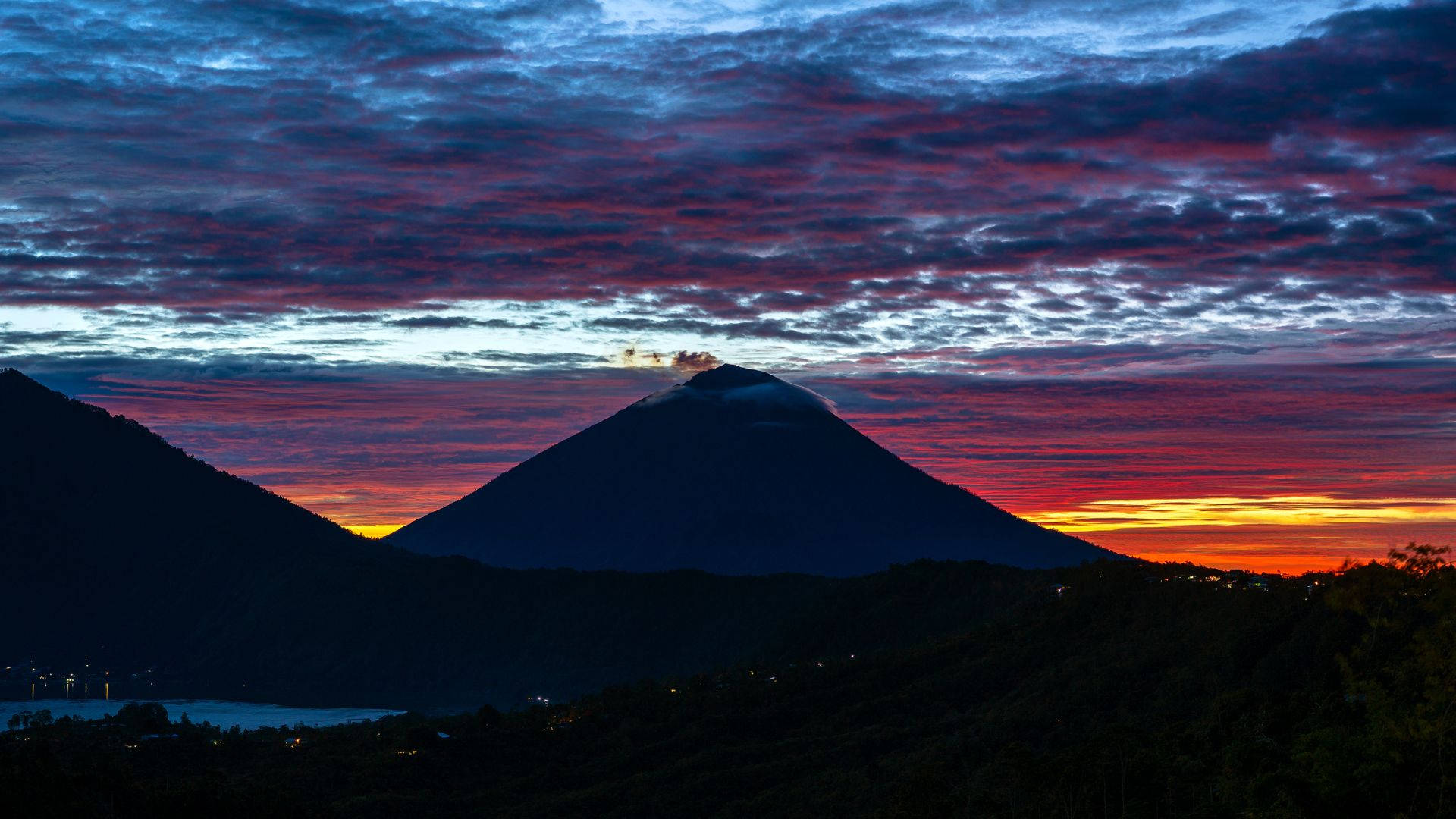 阿卡滕安哥火山山坡 壁紙 — 一座雄偉的火山山脈剪影矗立在火紅的日落天空前，天空佈滿紫色、橙色和藍色的雲彩。