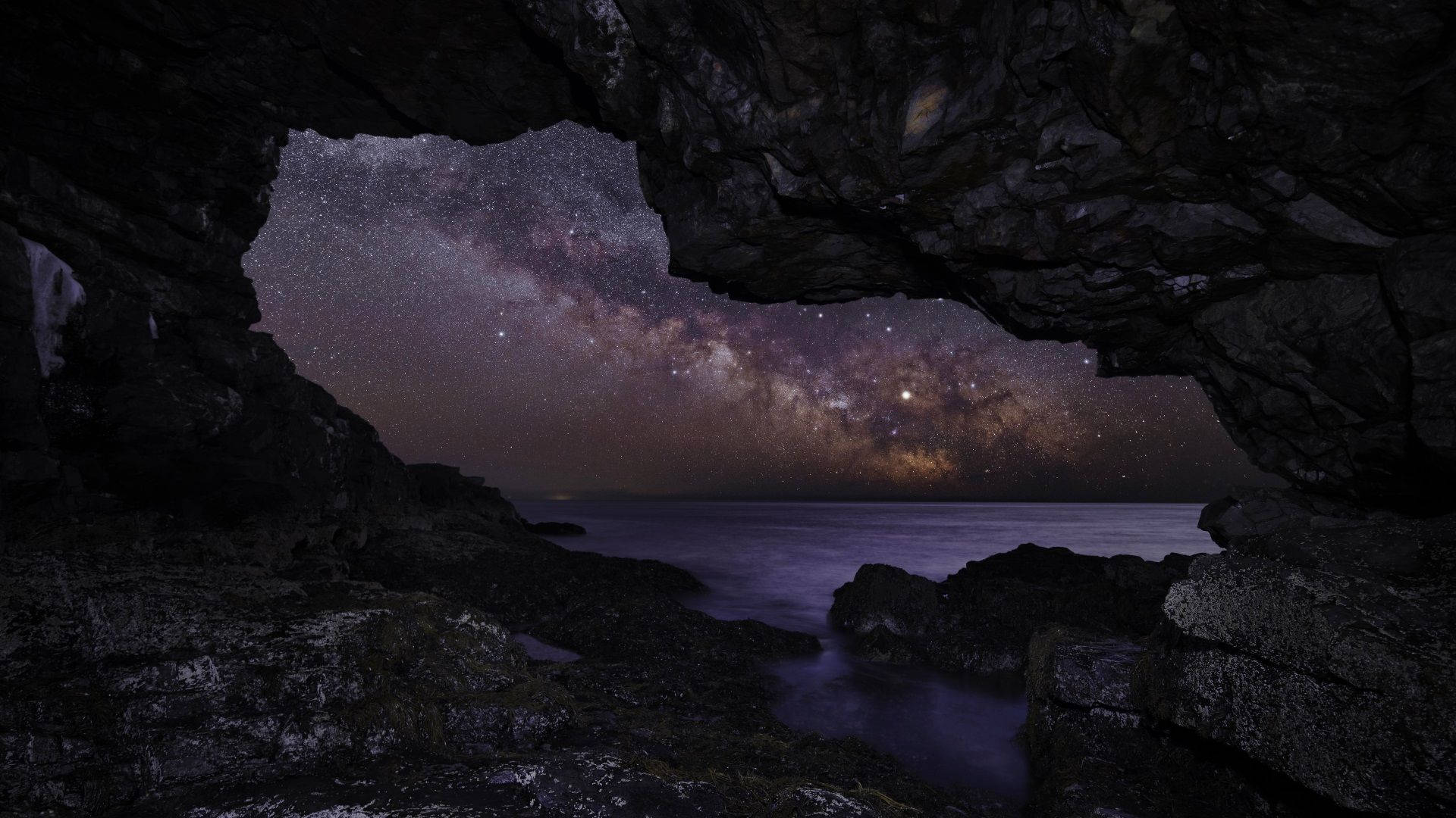 夜晚透過岩石洞穴開口在海面上看到的銀河系。