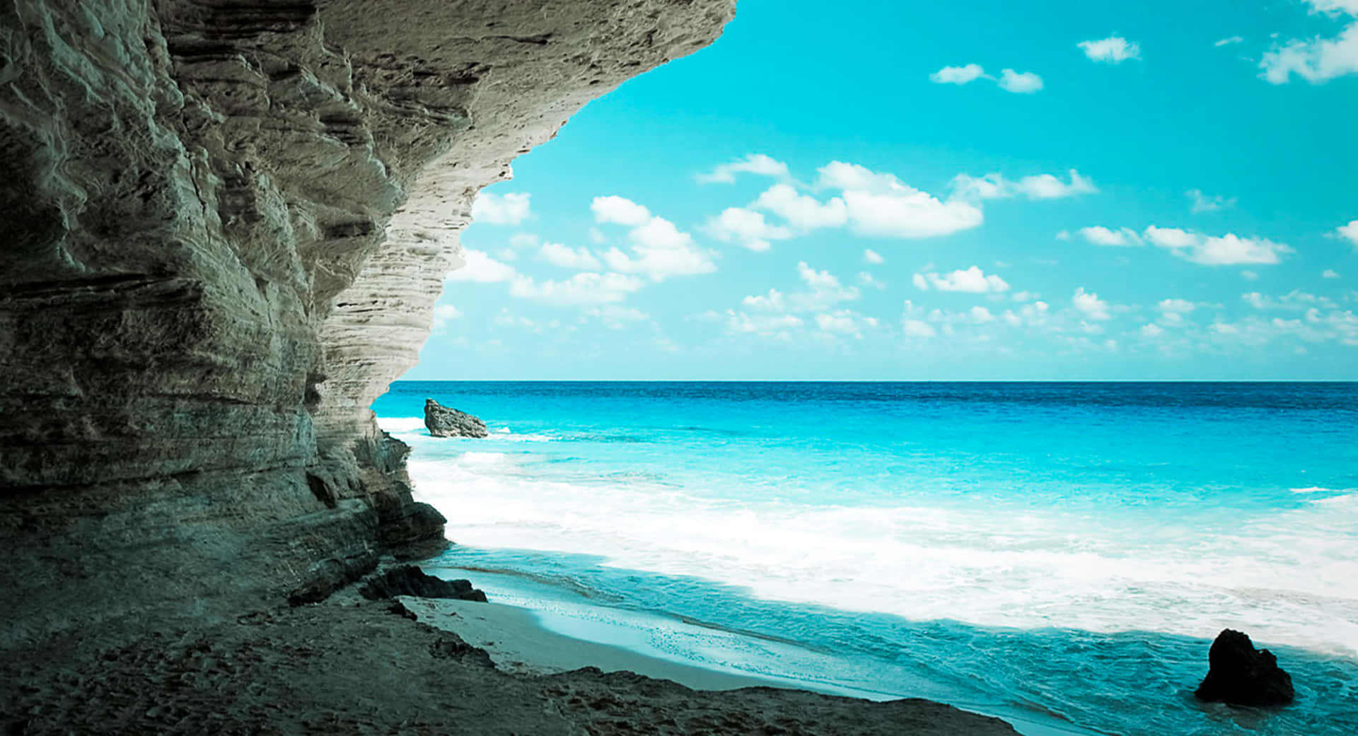 從懸崖洞穴俯瞰碧綠色的海浪和沙灘，天空湛藍。