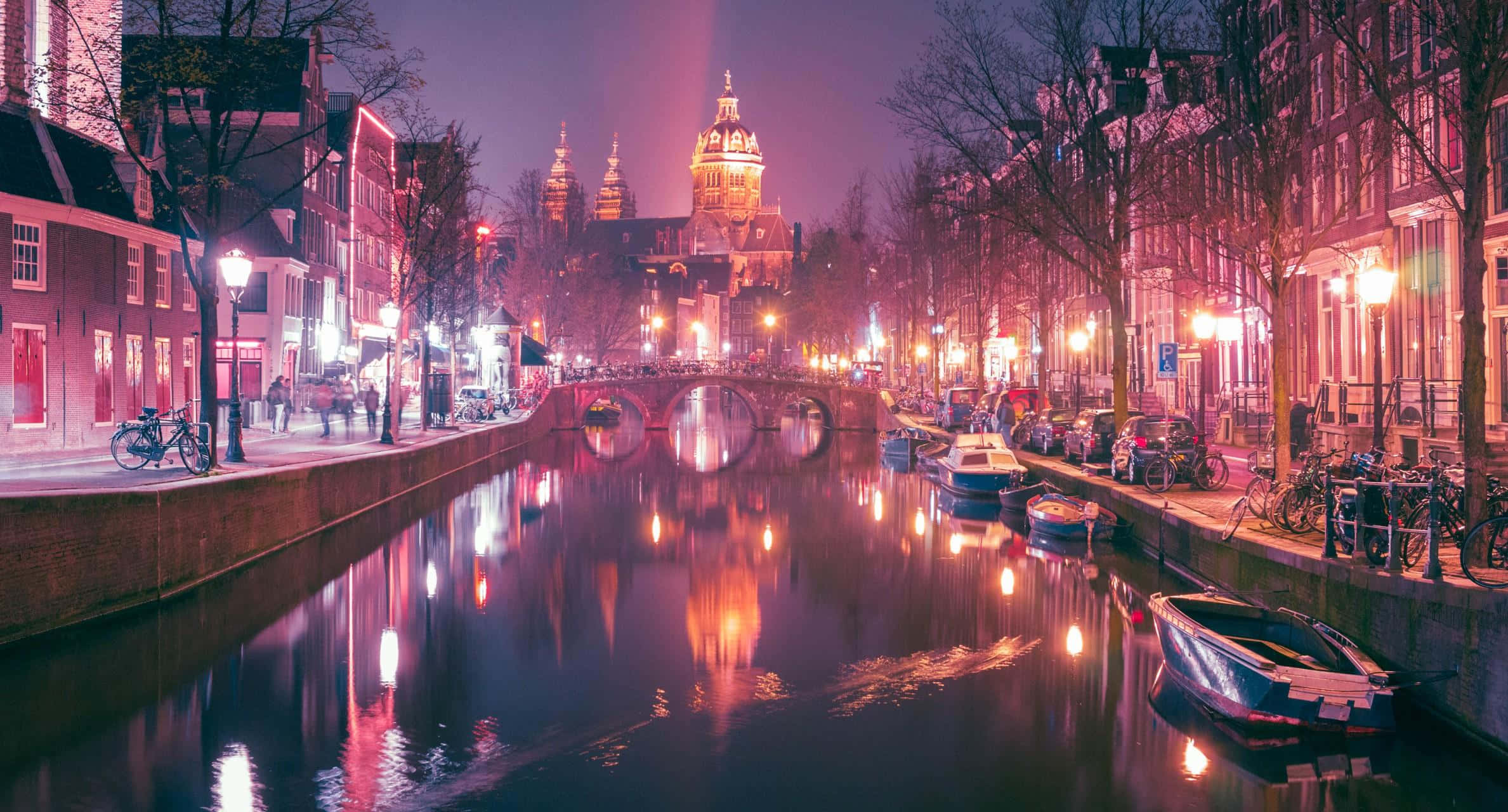 Red Light District 桌布 壁紙 — 阿姆斯特丹運河的充滿活力的夜景，發光的燈光反射在水面上，歷史建築沿著河岸排列。