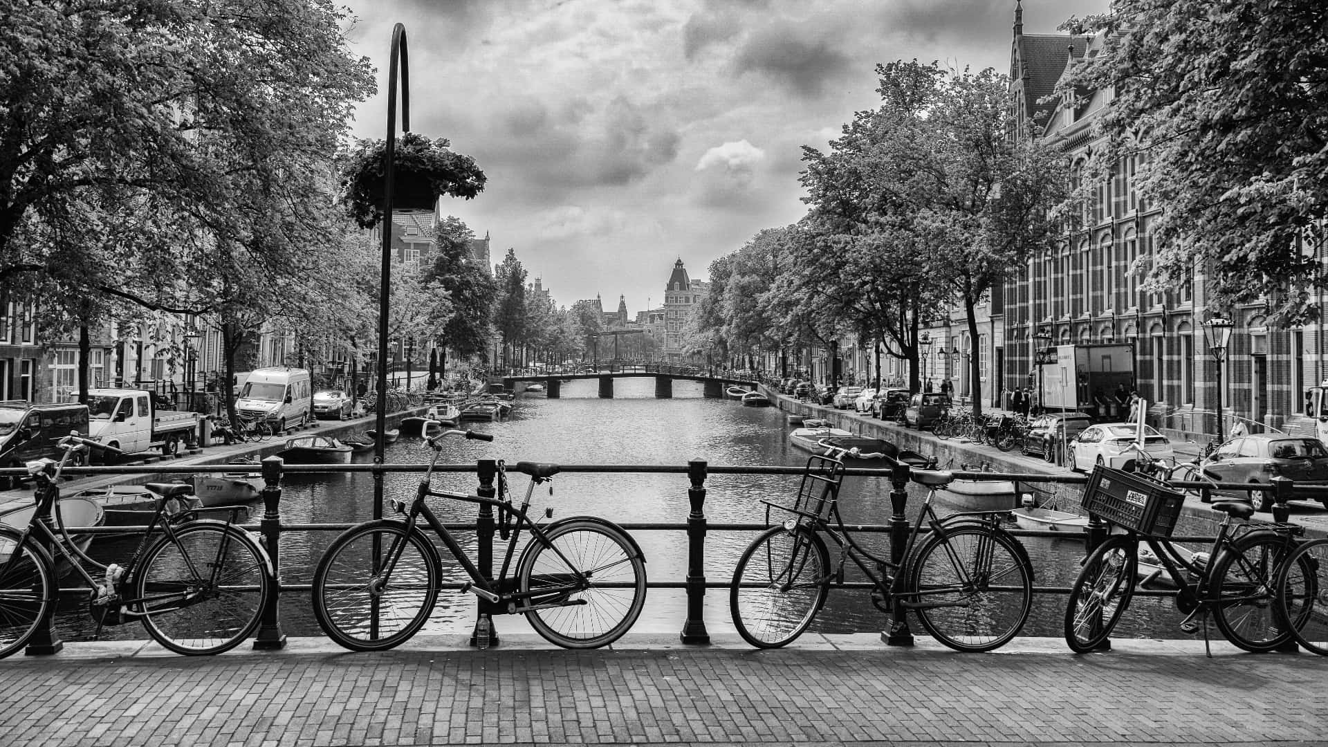 Black And White Cityscape 桌布 壁紙 — 阿姆斯特丹運河的黑白景觀，單車沿著磚砌小路排列，天空多雲。