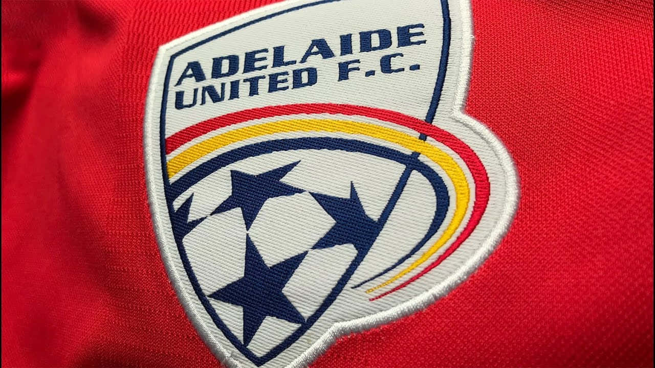Adelaide United 桌布 壁紙 — 阿德萊德聯足球會刺繡會徽喺紅色足球波衫布料上嘅特寫。