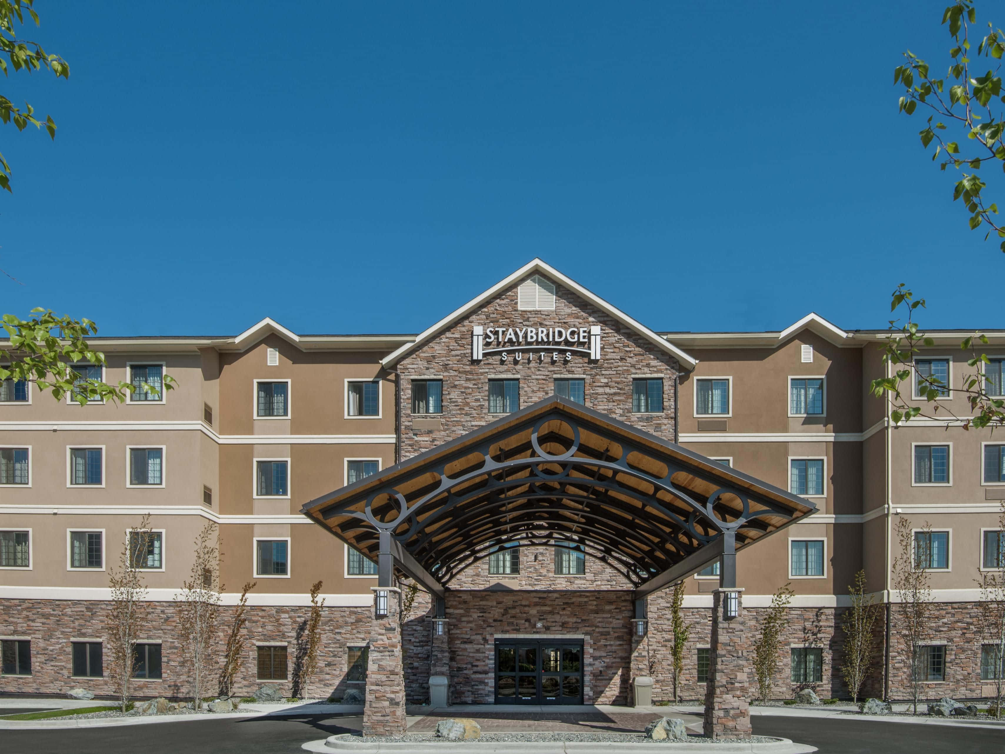 阿拉斯加安克雷奇Staybridge Suites酒店 壁紙 — 一座現代化的Staybridge Suites酒店建築，在晴朗的藍天下，設有石頭和木材的門廊入口。