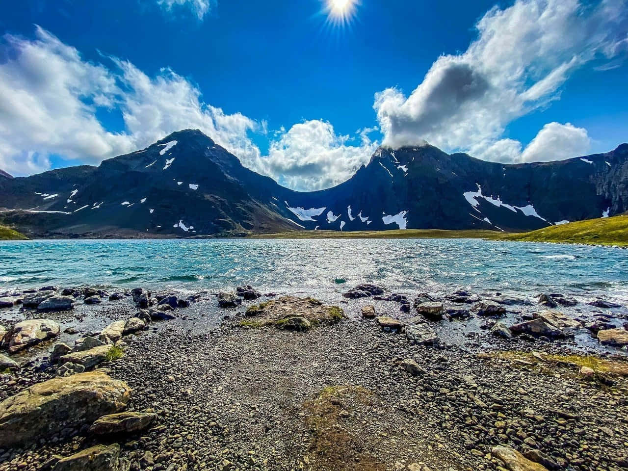 阿拉斯加安克雷奇兔子湖風景 壁紙 — 明亮的陽光照耀著一個藍綠色的湖泊，周圍是白雪覆蓋的山脈和岩石海岸，藍天白雲。
