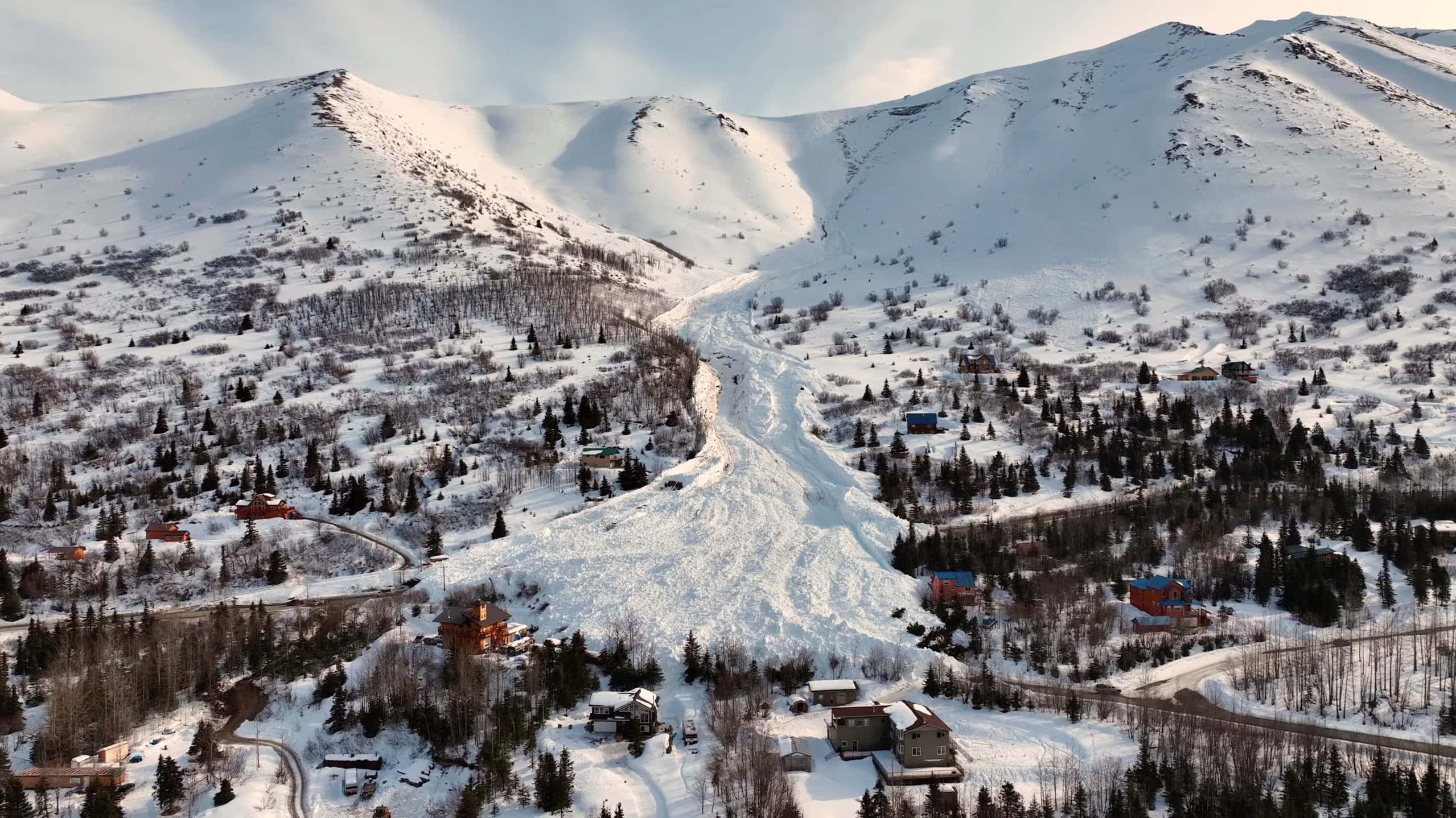 阿拉斯加安克雷奇雪峰小鎮風景 壁紙 — 白雪覆蓋的山谷鳥瞰圖，蜿蜒的滑雪道和散落在常綠樹林中的小屋。