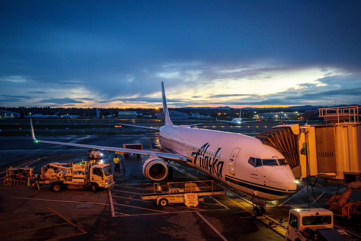 黃昏時機場閘口的阿拉斯加航空飛機及地勤人員和設備。