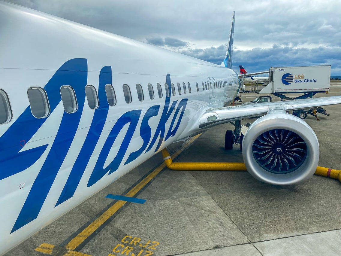 阿拉斯加航空公司飛機停泊在機場閘口，附近有貨車。