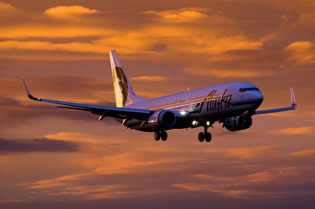 阿拉斯加航空飛機在日落時分降落，伴有橙色雲彩