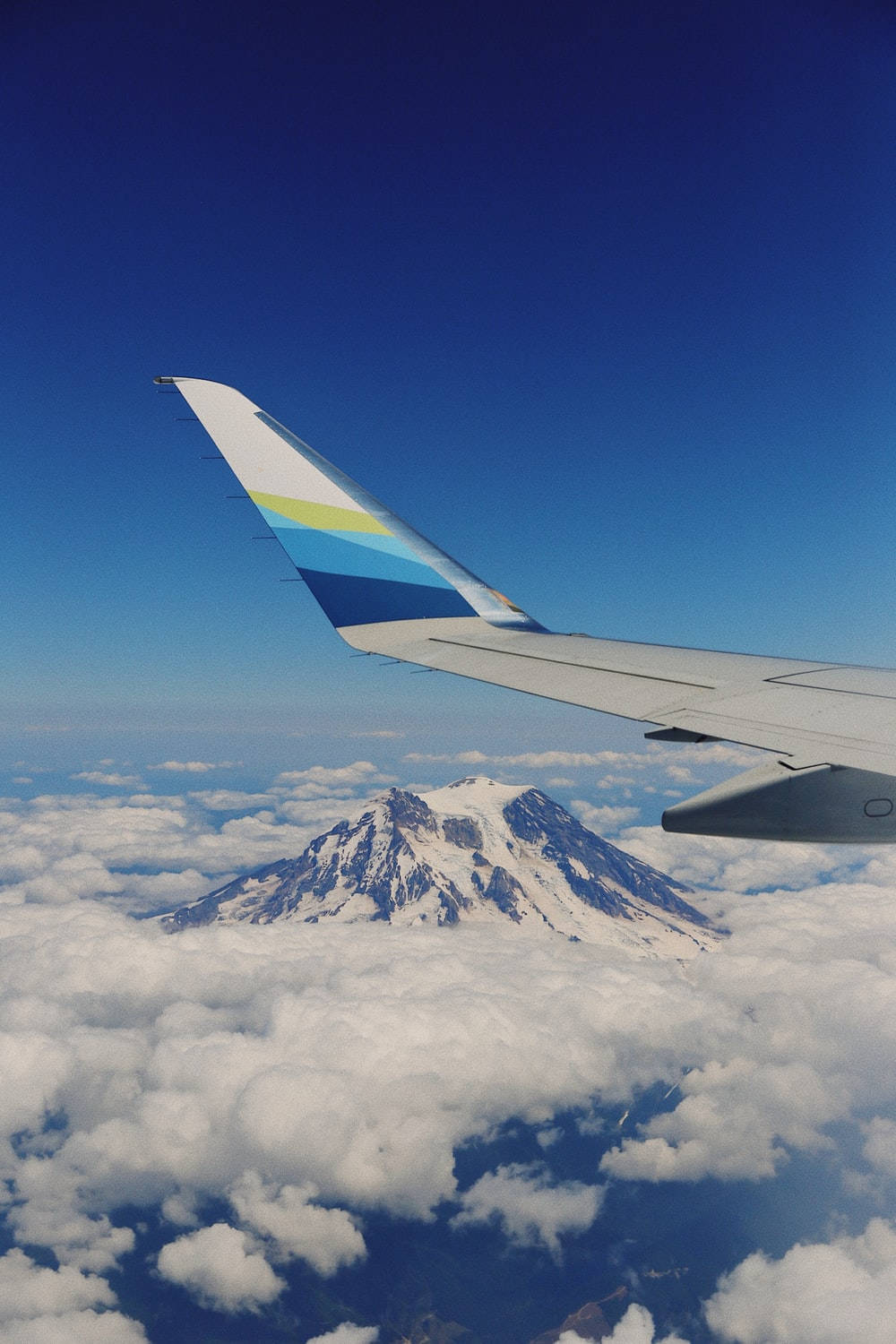 雲層上的飛機機翼，下方可見積雪的山峰。