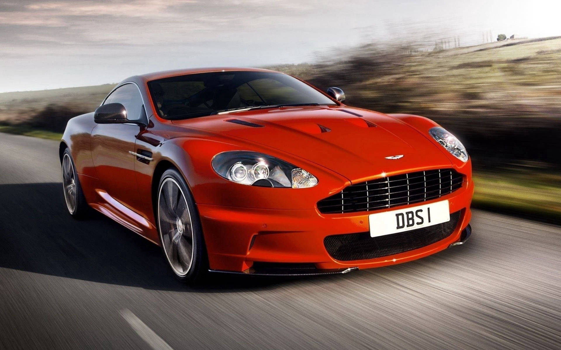 紅色Aston Martin DBS在日落時分在風景優美的道路上疾馳。