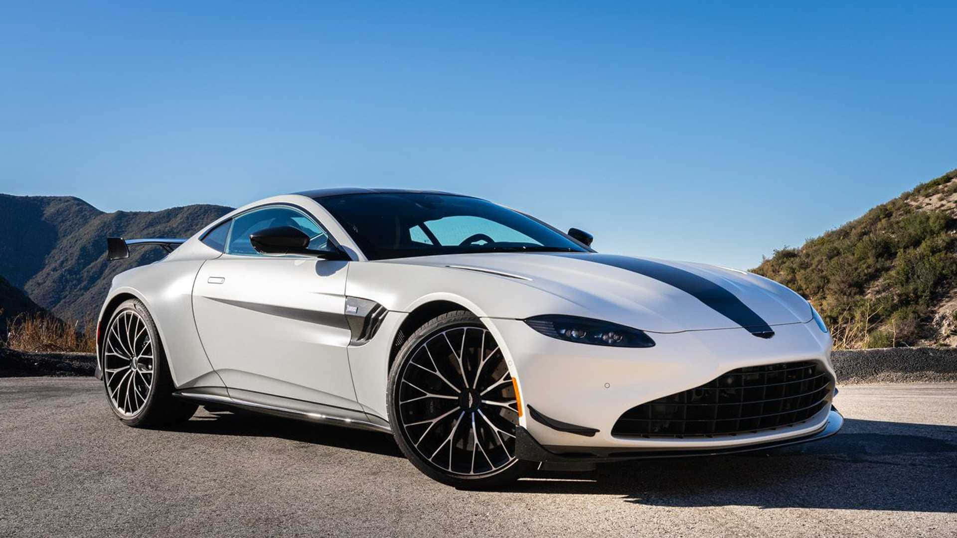 阿斯頓·馬丁 V8 Vantage 壁紙 — 一架時尚的白色Aston Martin跑車帶有黑色賽車條紋，停在藍天白雲下的山路上。