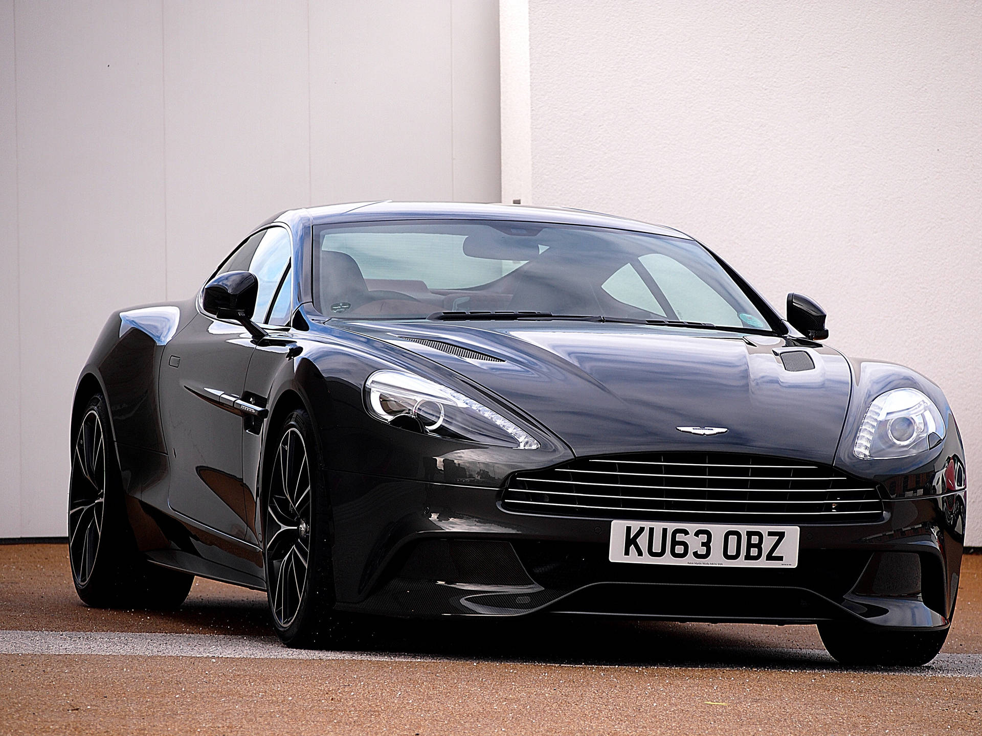 黑色Aston Martin跑車停在白色牆壁前。