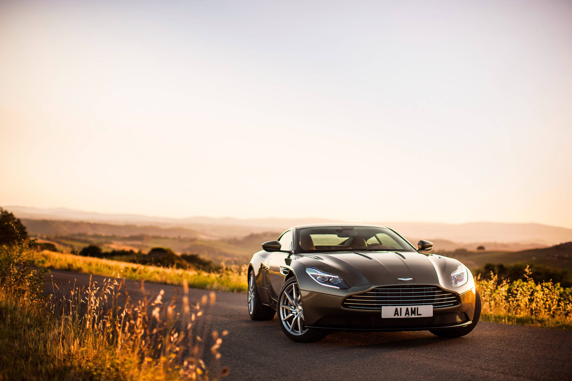 夕陽下風景如畫的鄉村道路上的銀色Aston Martin DB11。