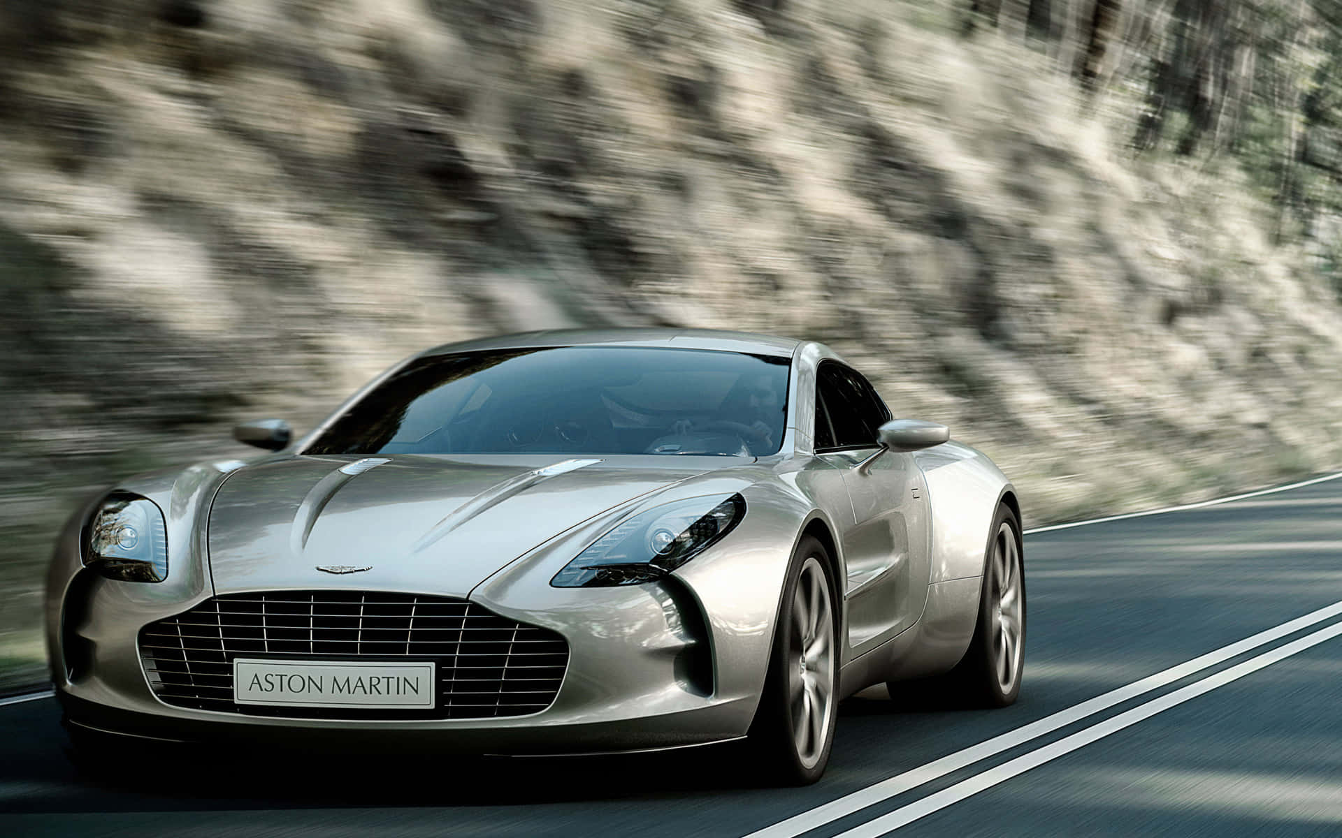 阿斯頓·馬丁：經典跑車 壁紙 — 一輛銀色Aston Martin跑車沿著蜿蜒的山路疾馳，背景是模糊的岩石懸崖。