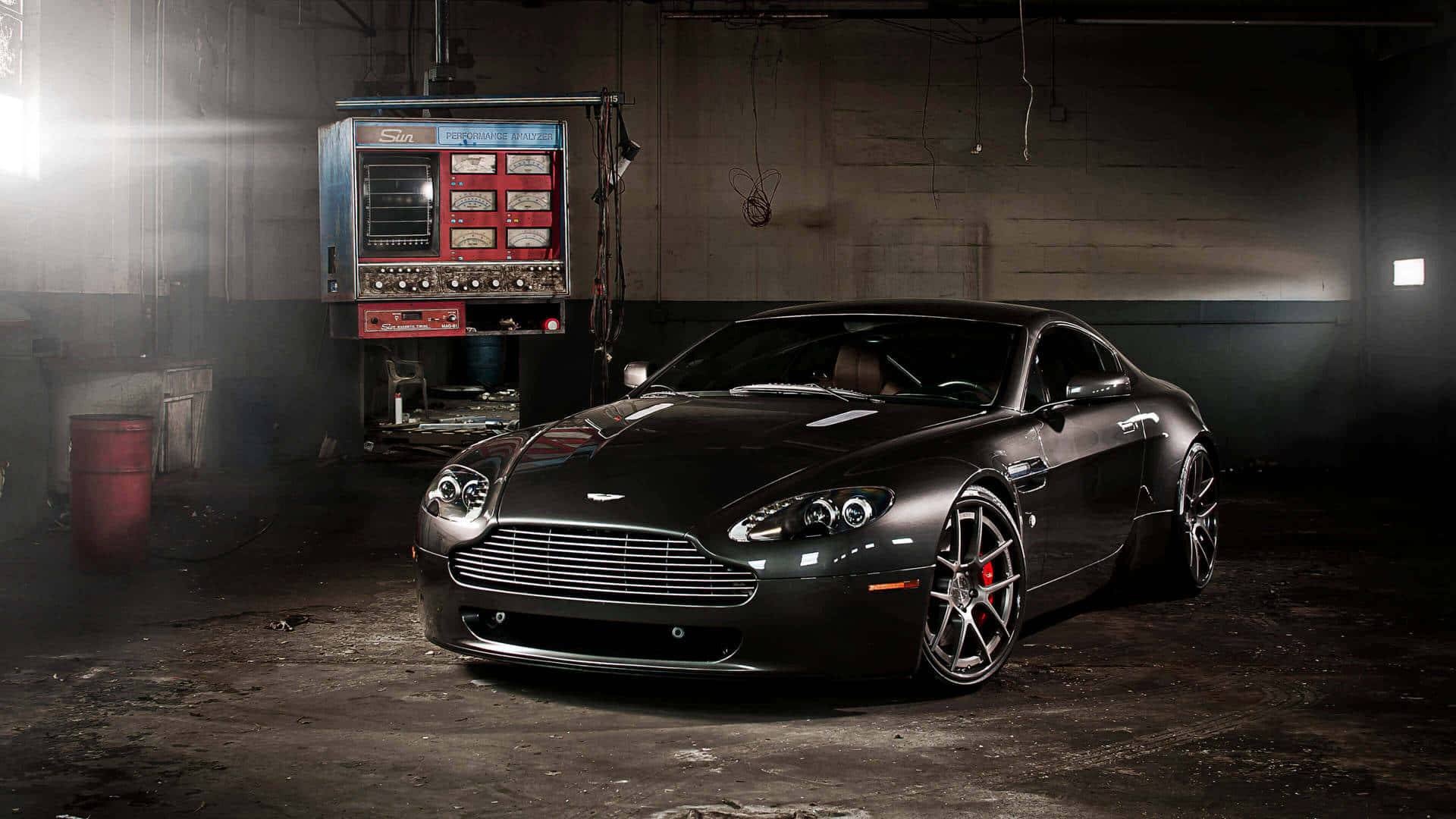 阿斯頓·馬丁Vantage——頂級豪華跑車 壁紙 — 一輛時尚的啞光黑色阿斯頓馬丁跑車在粗獷的工業車庫中，在戲劇性的聚光燈下閃閃發光。