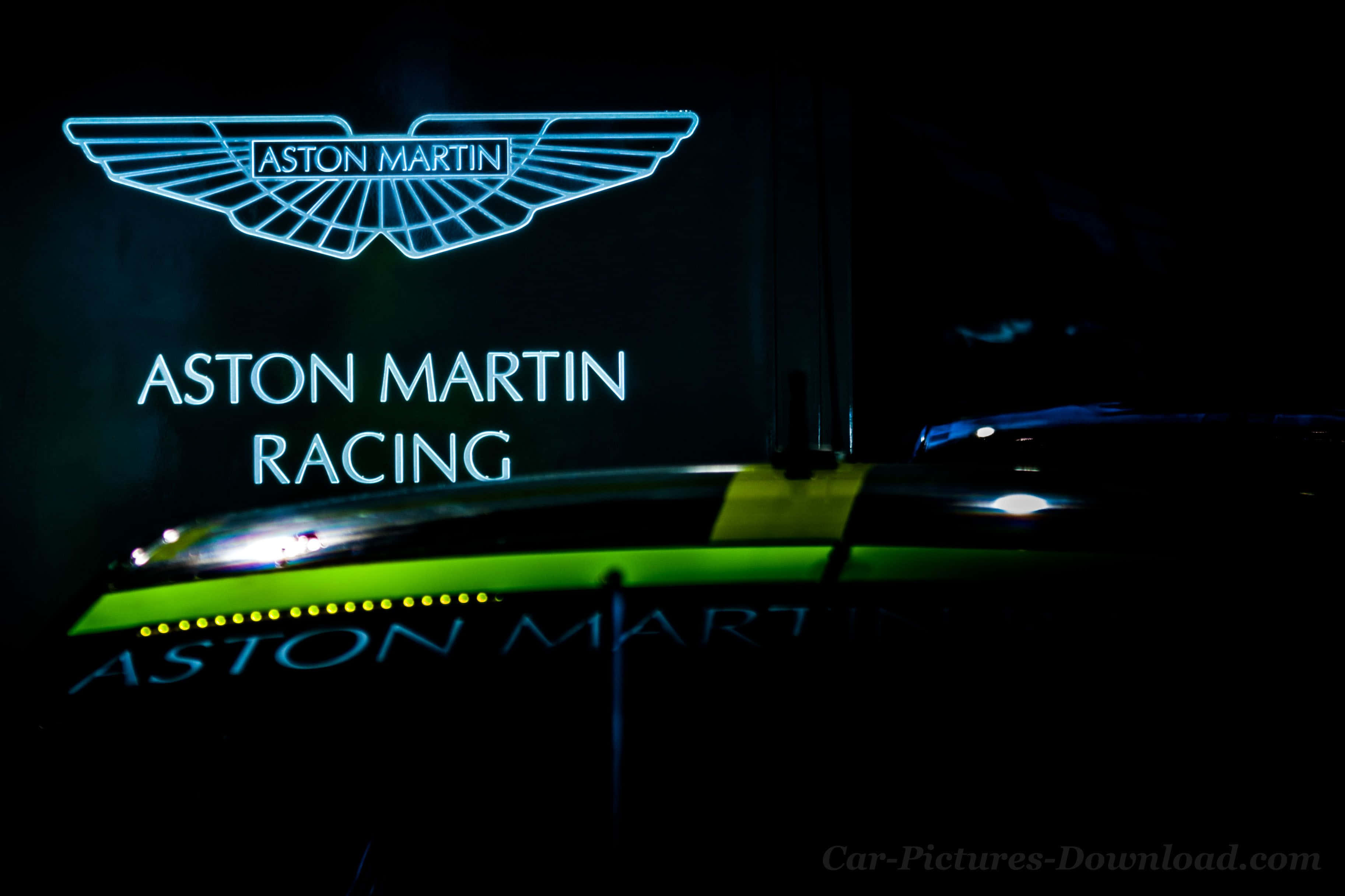 阿斯顿·马丁經典外觀 壁紙 — 一個發光的藍色Aston Martin Racing霓虹燈牌在夜晚照亮了一輛時尚的綠色賽車。