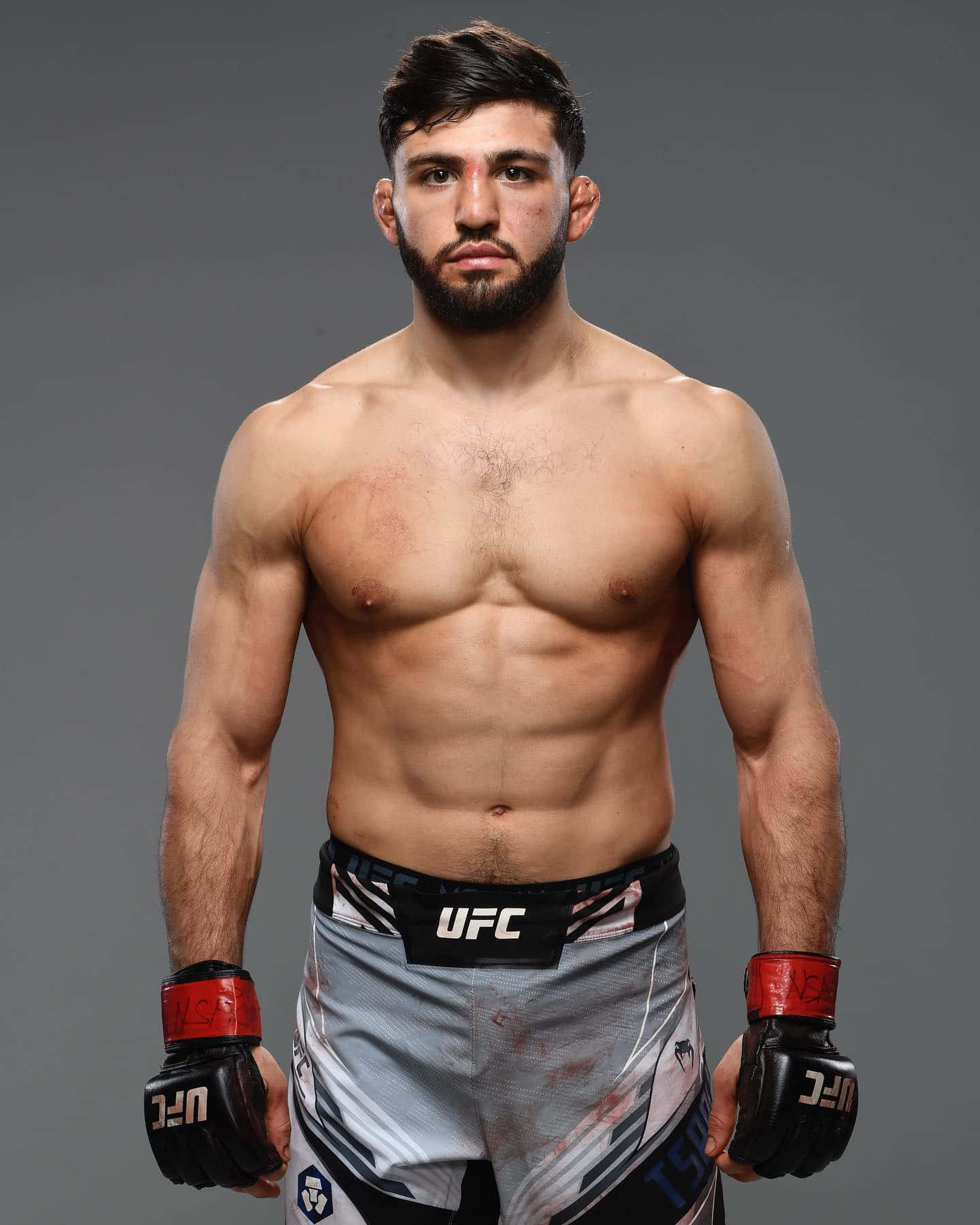 一位赤裸上身的男性MMA拳手，穿著UFC短褲和手套，為工作室肖像擺姿勢。