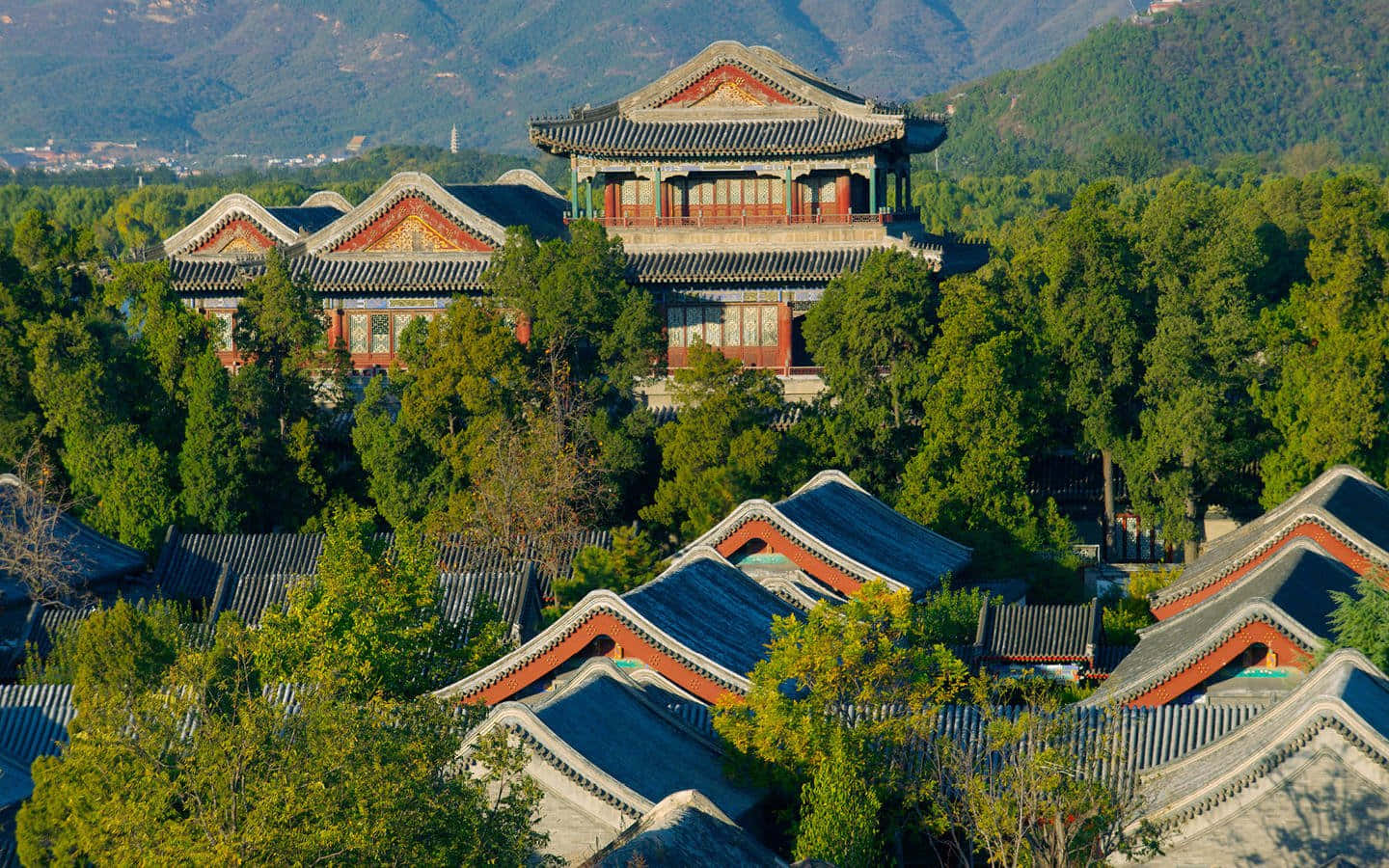阿曼夏日宮殿全景 壁紙 — 傳統中式宮殿建築，擁有彎曲的瓦片屋頂，坐落在茂密的綠樹之間，以山巒為背景。
