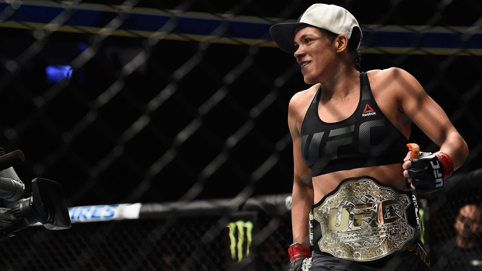 女性MMA拳手在八角籠內手持冠軍腰帶慶祝勝利。