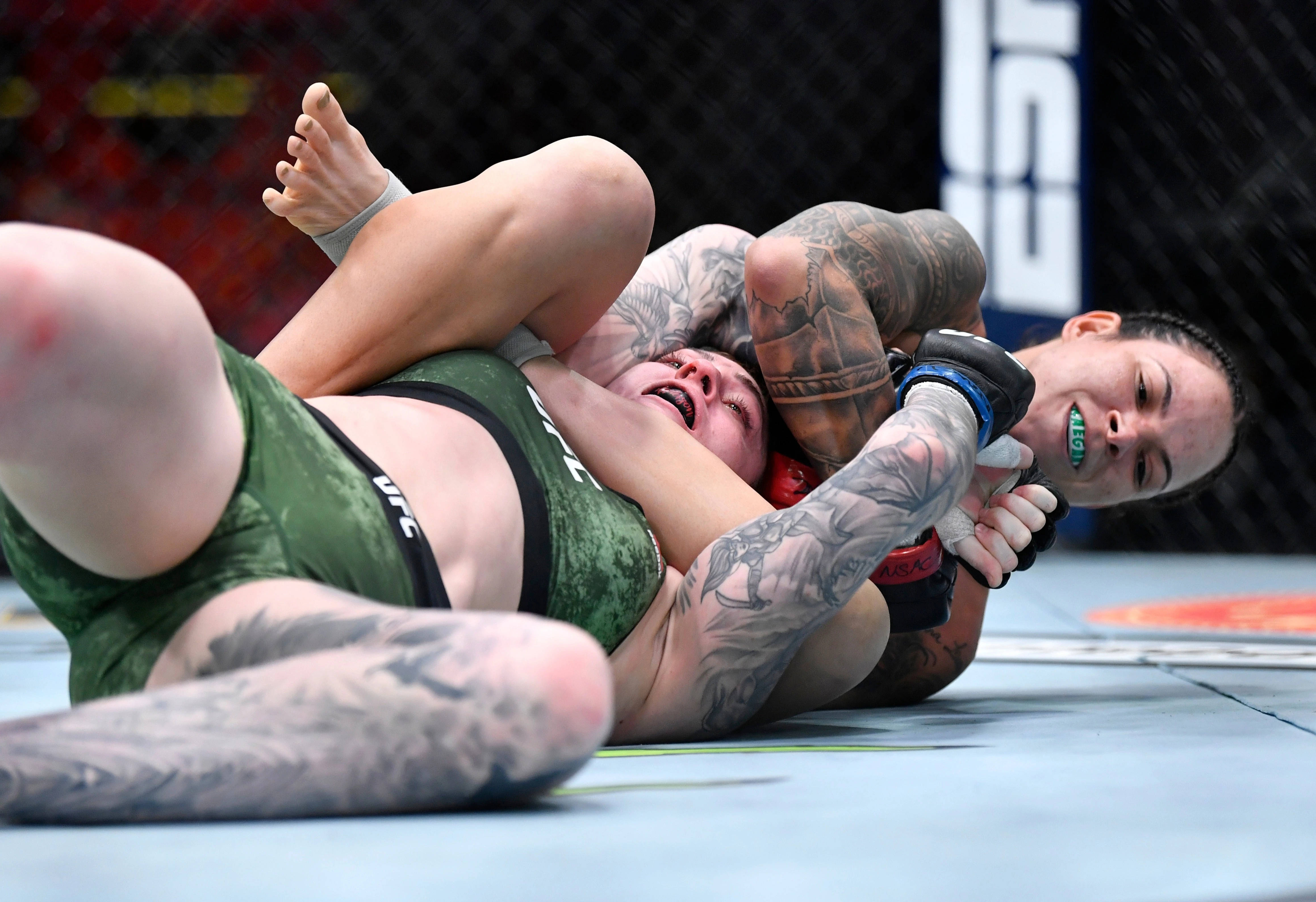 阿曼達·努內斯抱摔對手 壁紙 — 兩名女性MMA拳手在藍色八角形墊上激烈纏鬥，其中一人施展鎖喉技。