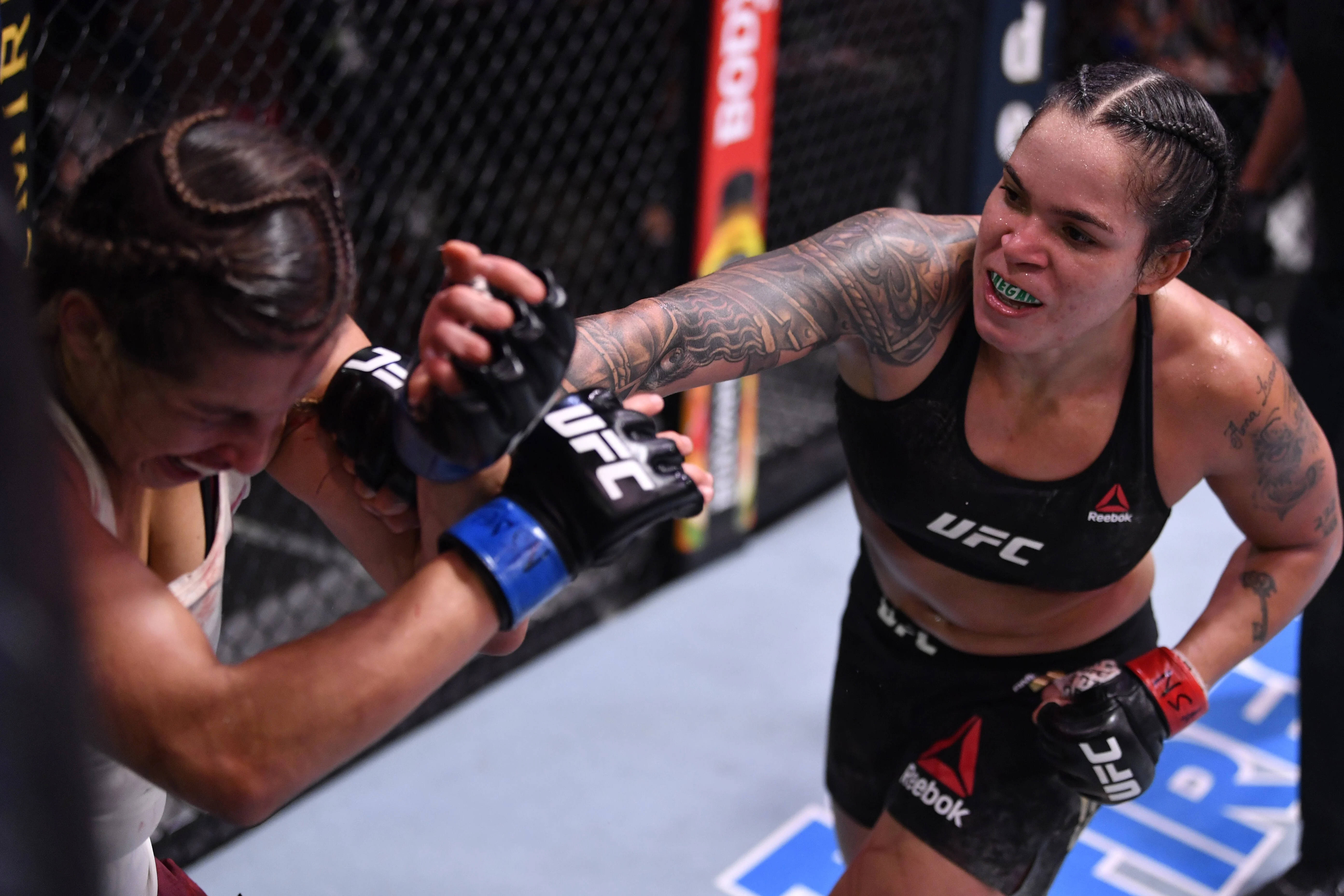 阿曼達·努內斯擊打對手臉部 壁紙 — 兩名女性MMA拳手在UFC八角籠內激烈纏鬥，帶有紋身和專注的表情。