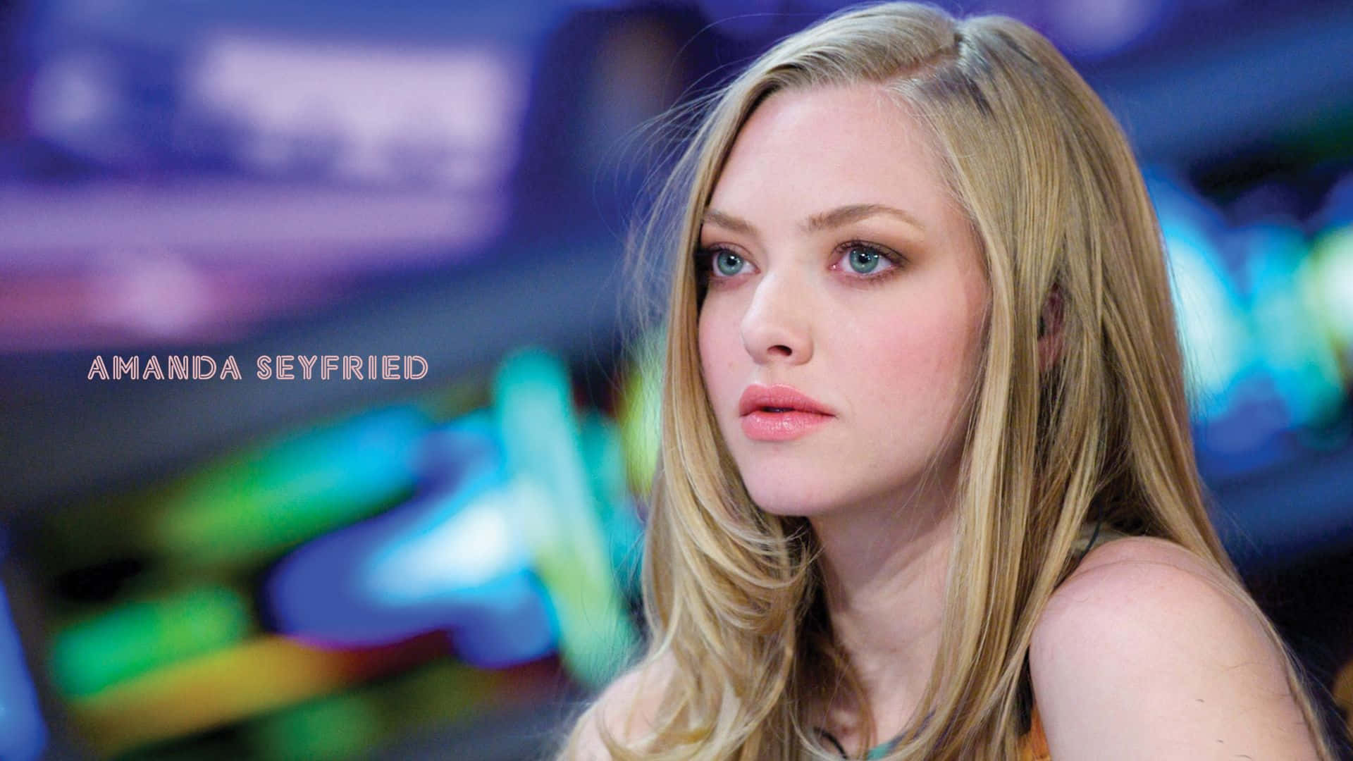 Amanda Seyfried 桌布 壁紙 — 阿曼達·西耶弗里德在充滿活力的模糊霓虹背景前沉思，背景帶有冷色調的藍色和綠色。