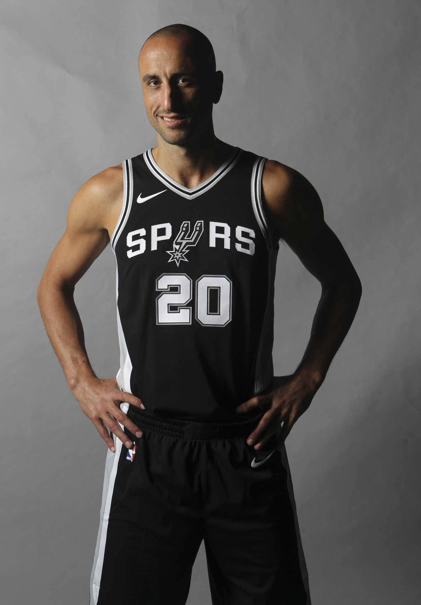 阿根廷NBA球員馬努·吉諾比利 壁紙 — 一位光頭籃球運動員身穿黑色馬刺隊20號球衣，雙手叉腰，自信地站在灰色攝影棚背景前。
