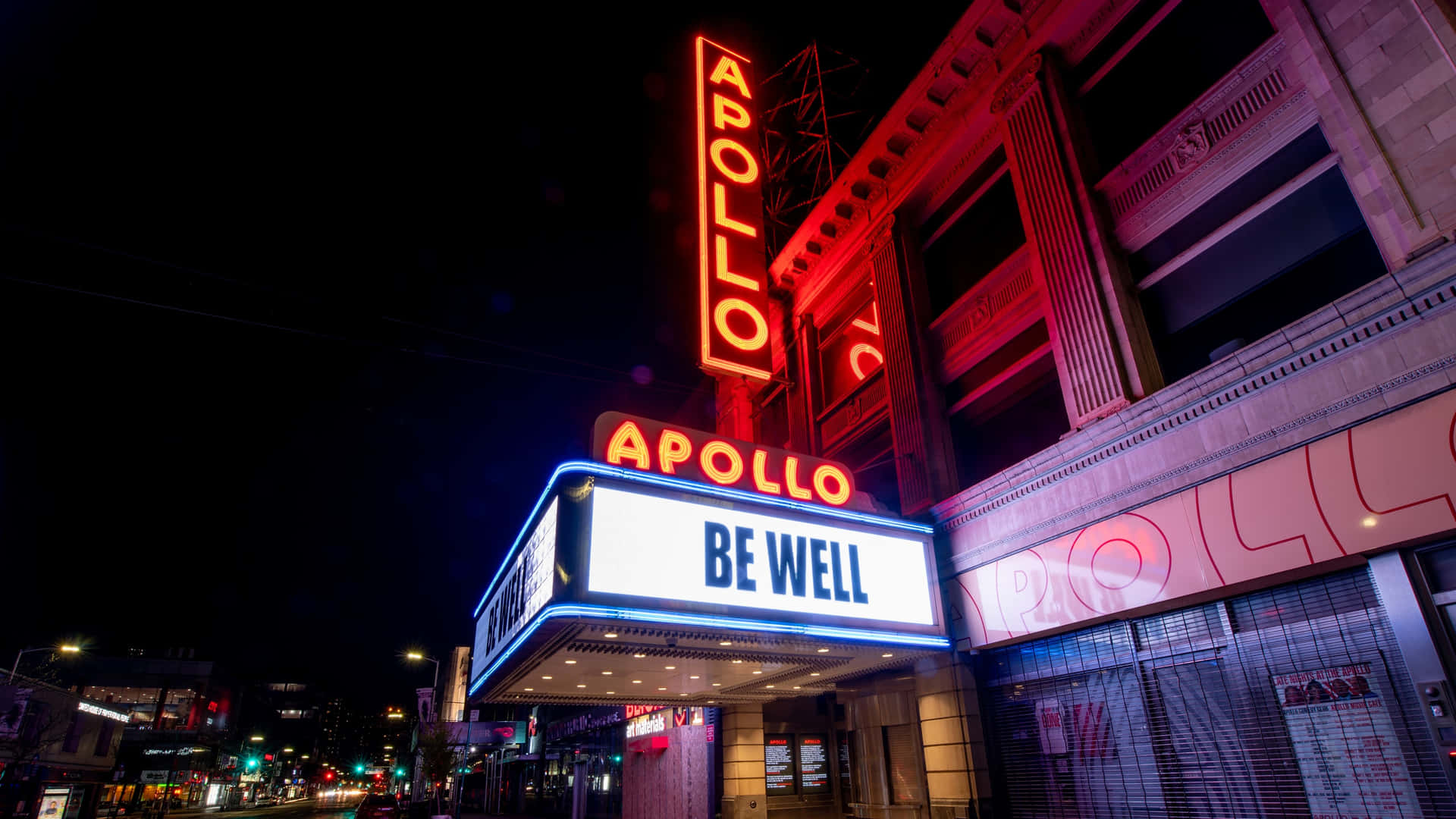 阿波羅劇院簷篷在夜晚發出紅藍光芒，帶有「BE WELL」訊息。