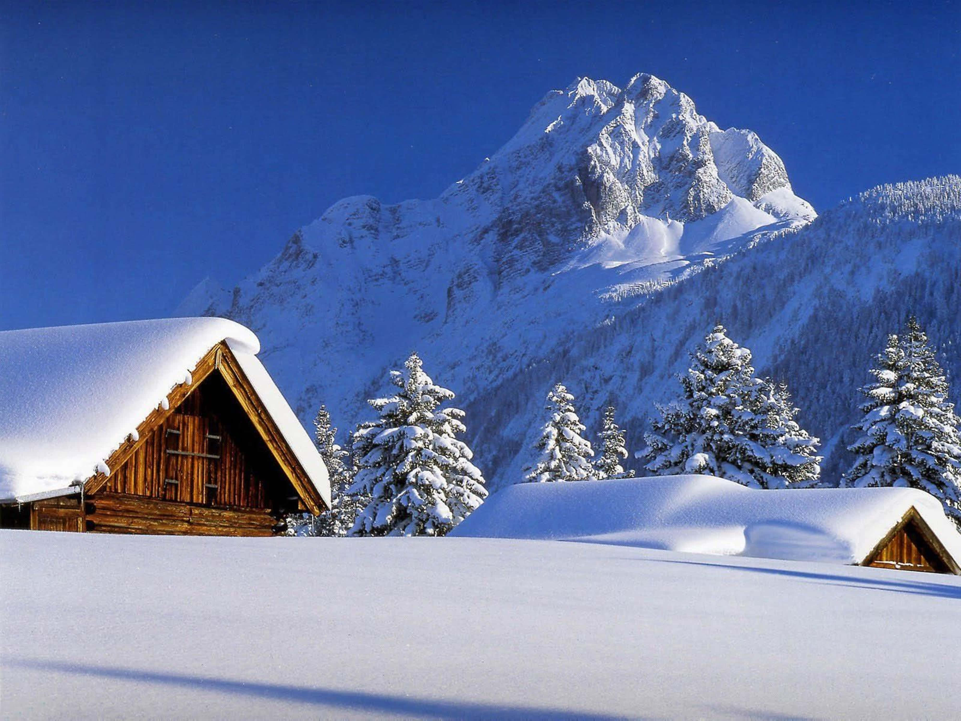 阿爾卑斯山區雪覆木屋 4K 壁紙 — 被雪覆蓋的木屋坐落在晴朗藍天下寧靜的冬季山谷中。