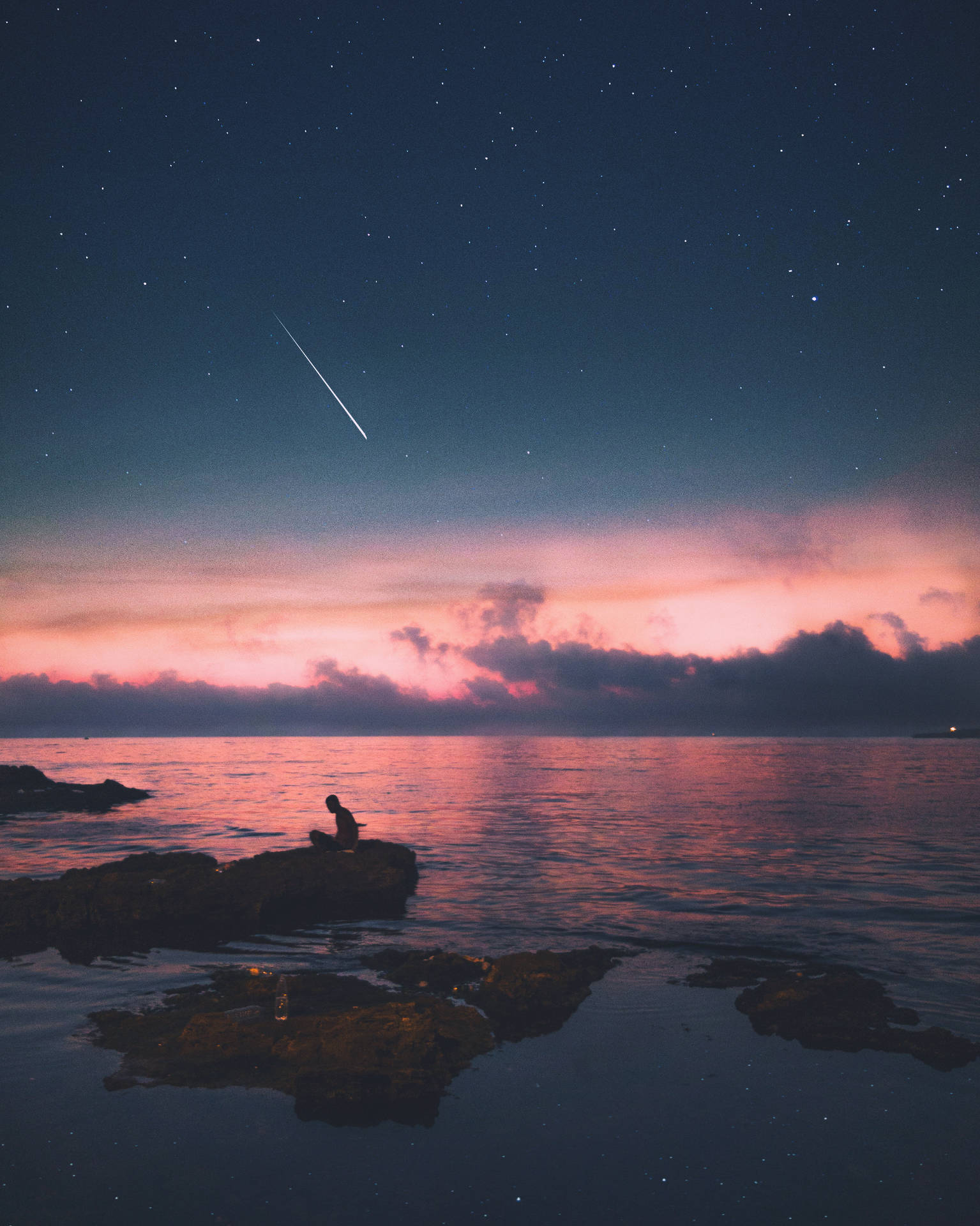人坐在岩石上觀看夜間海洋上空的流星雨。