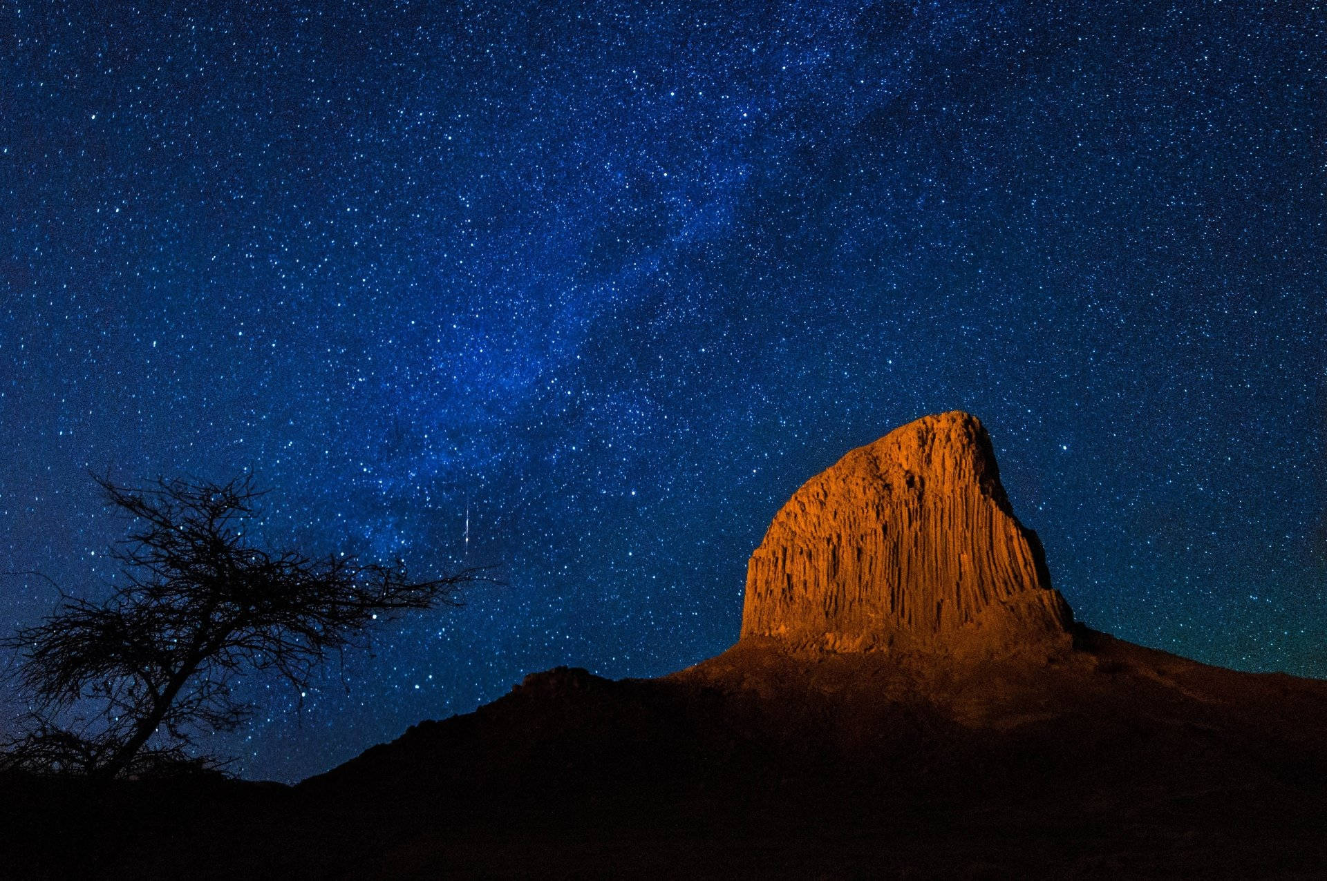 阿爾及利亞霍格沙漠銀河 壁紙 — 一棵孤獨的樹在充滿活力的星空下形成剪影，銀河在發光的橙色岩石結構上拱起。