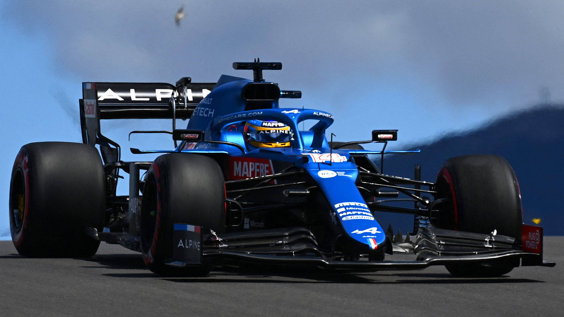 藍黑配色的Alpine F1賽車在賽道上疾馳，輪胎冒出煙霧。