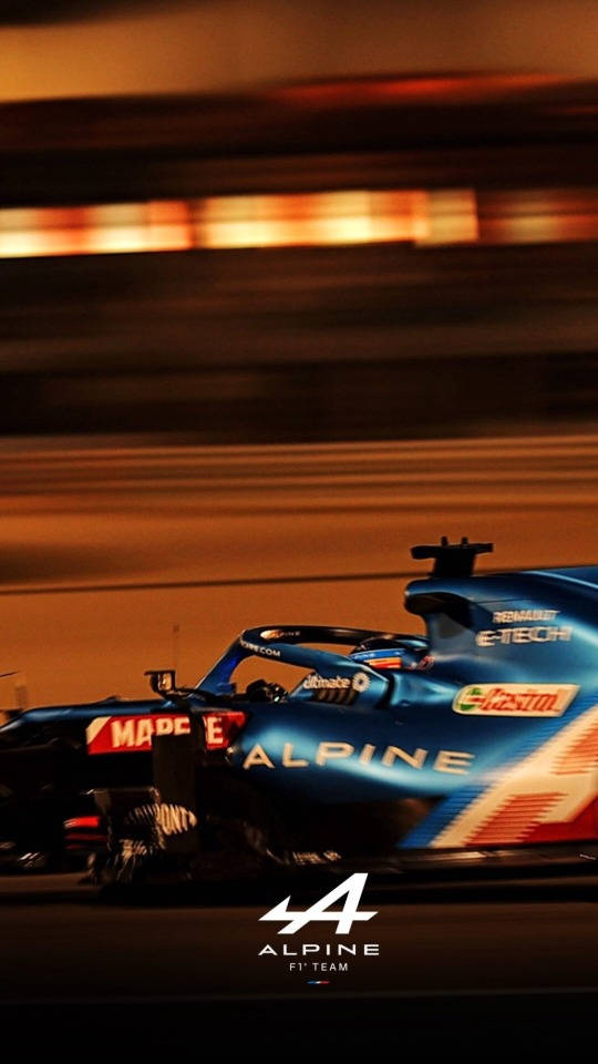 藍色 Alpine F1 賽車在夜間高速行駛，背景有模糊的橙色燈光。