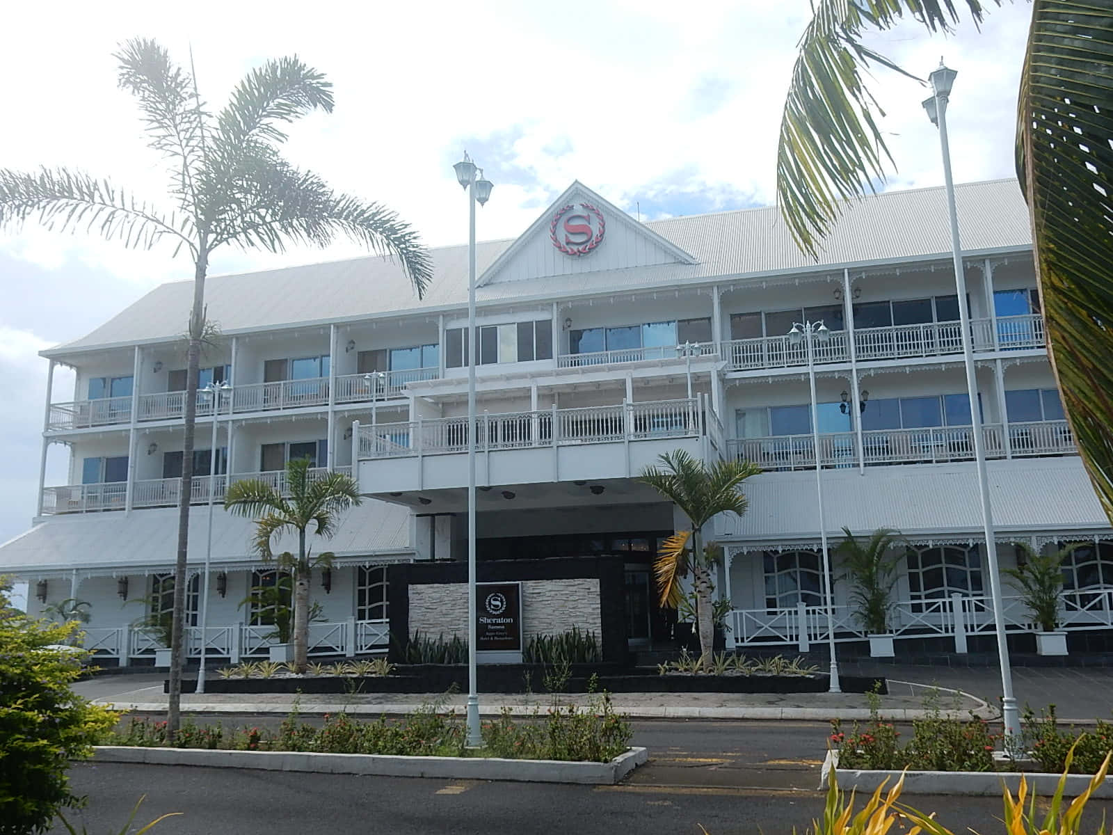 白色酒店建築，棕櫚樹和陽台，天空多雲。