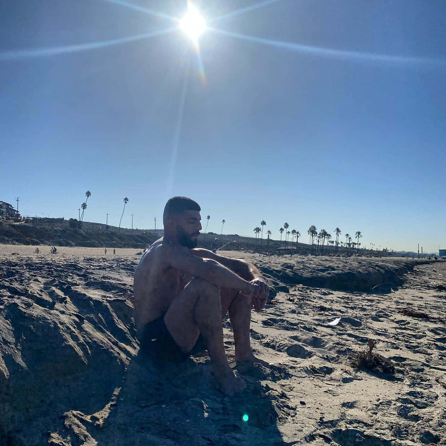 一個男人獨自坐在陽光明媚的海灘上，背景有棕櫚樹。