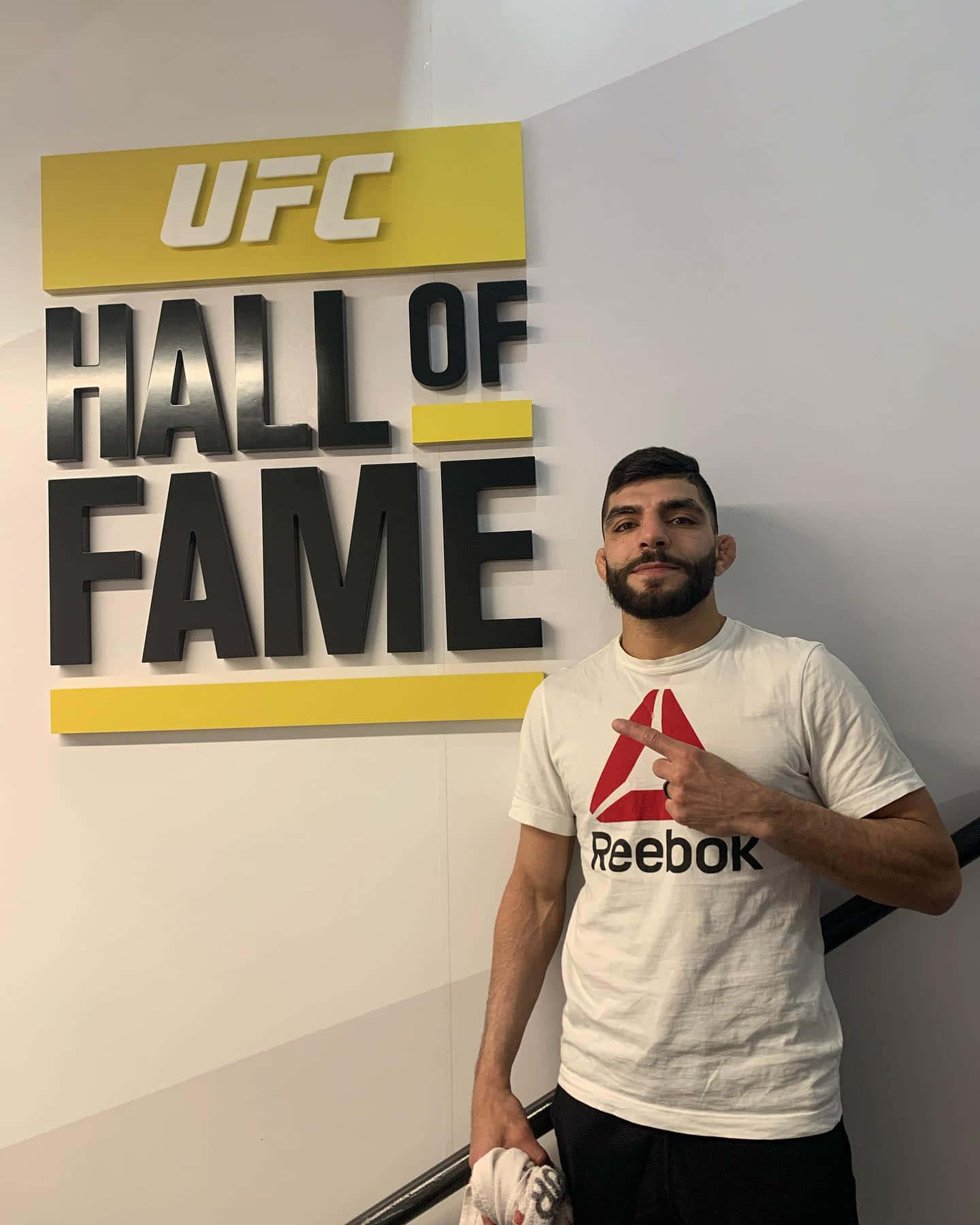 穿著Reebok襯衫的男人在室內指著UFC名人堂標誌。