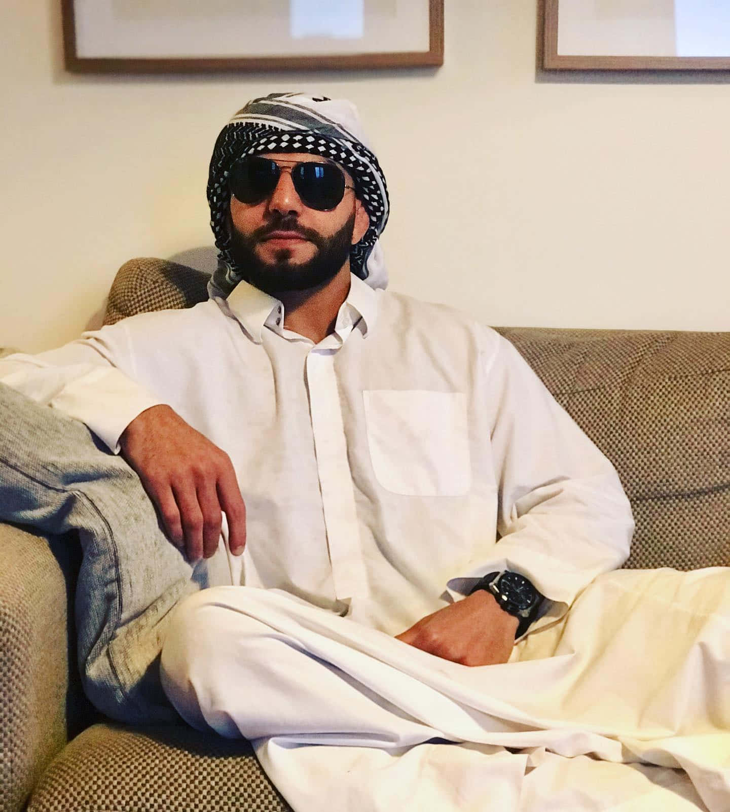 身穿白色傳統服飾和太陽眼鏡的男子坐在梳化上。