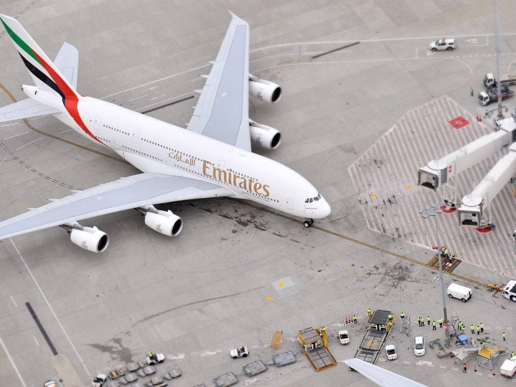 阿聯酋航空A380飛機停泊在機場閘口，有地勤人員和車輛。
