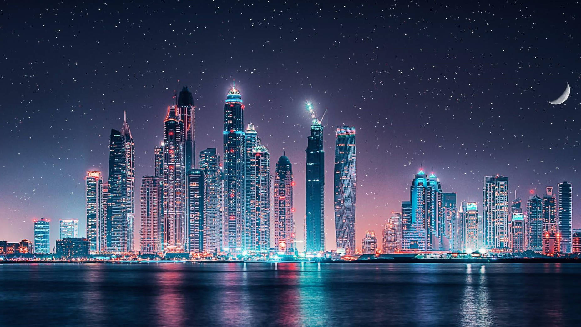 夜間城市景觀，摩天大樓燈火通明，星空倒映在水中。