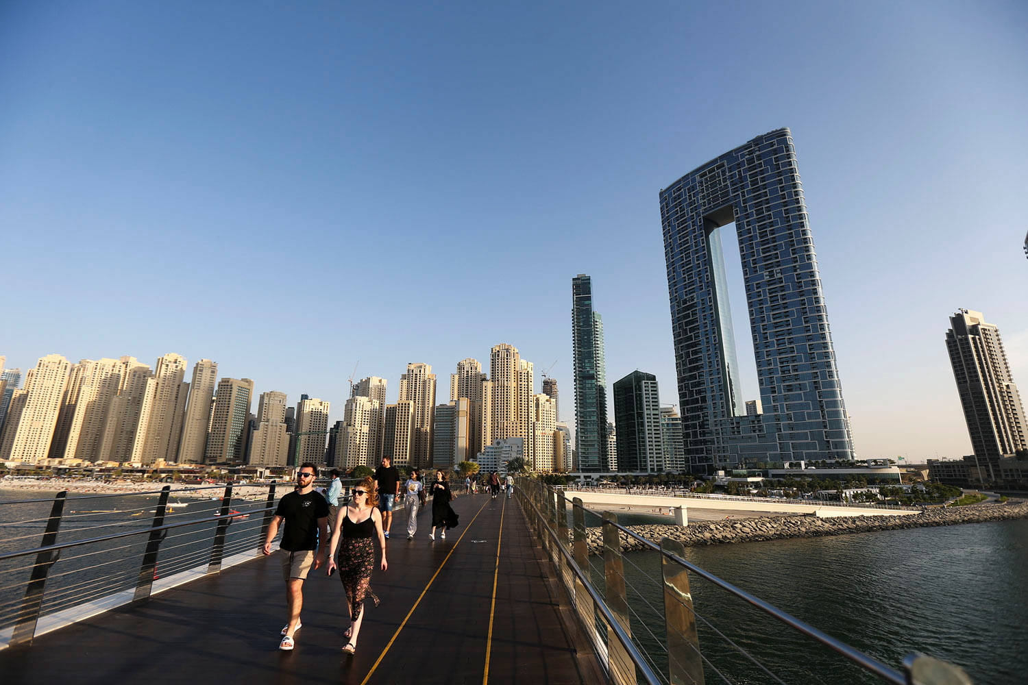 人們在水上橋上行走，身後是高聳的城市建築。