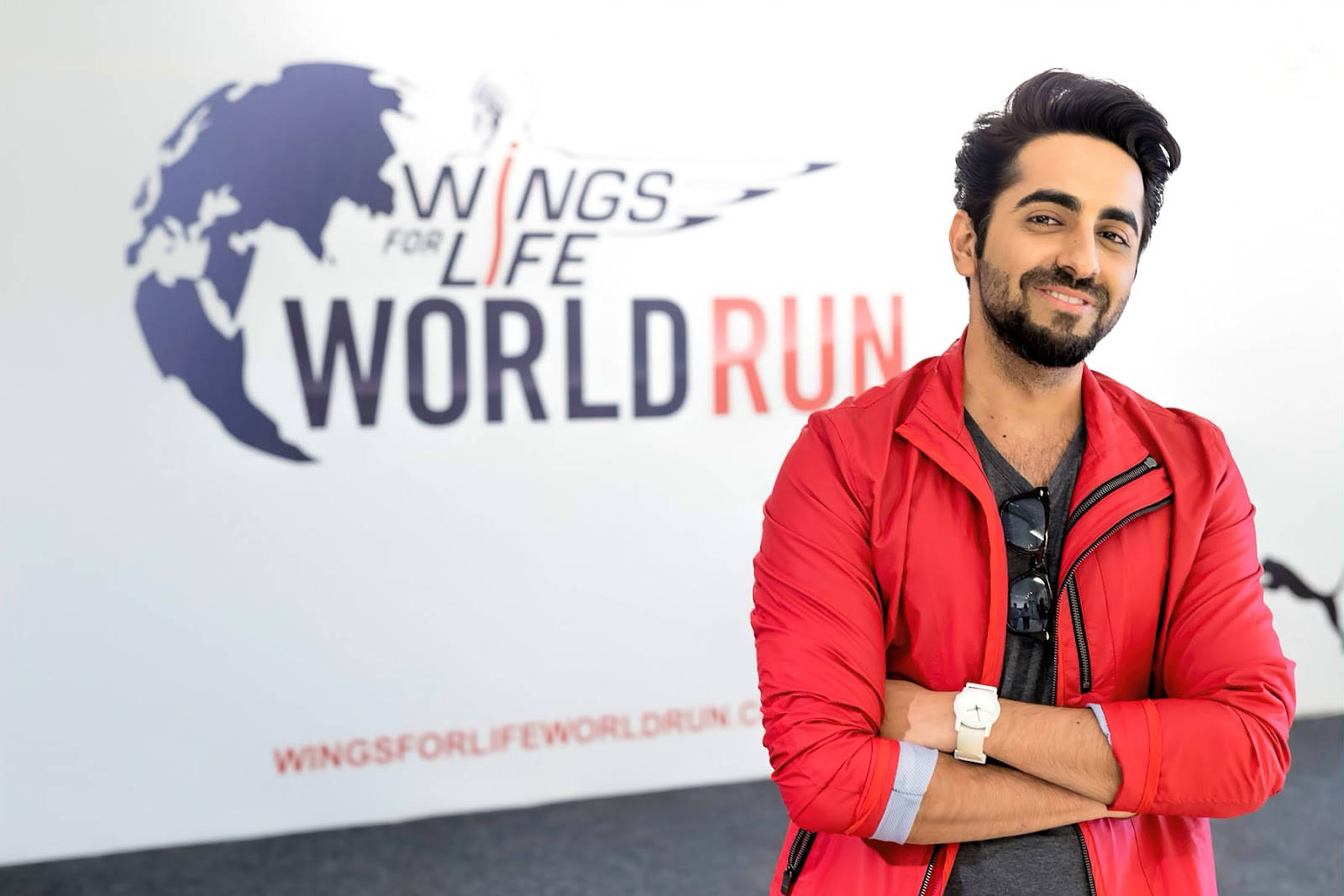 在Wings for Life World Run活動中，身穿紅色外套的男子對著鏡頭微笑。