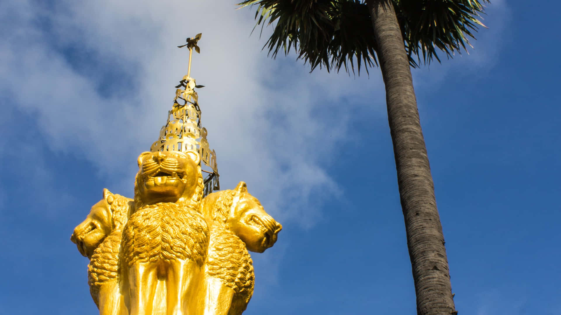 金色三頭獅子雕像在藍天下棕櫚樹旁
