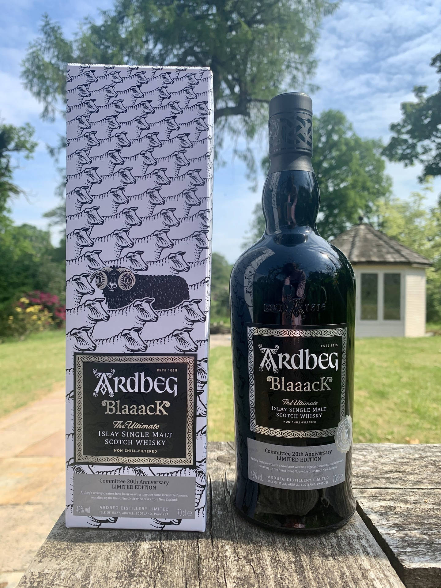 Ardbeg Blaaack威士忌瓶和盒子在戶外木桌上，配以綠意和天空。