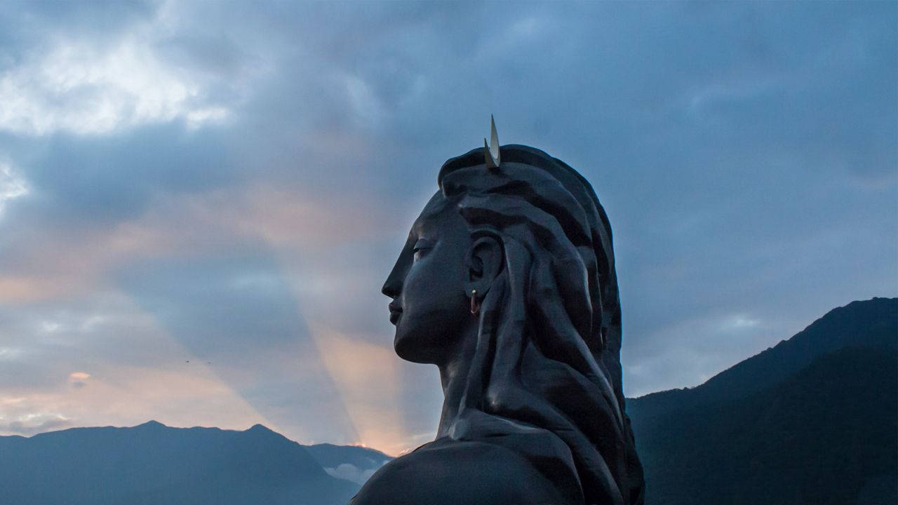 帶角女性雕像在暮色山巒和粉藍天空下的剪影。