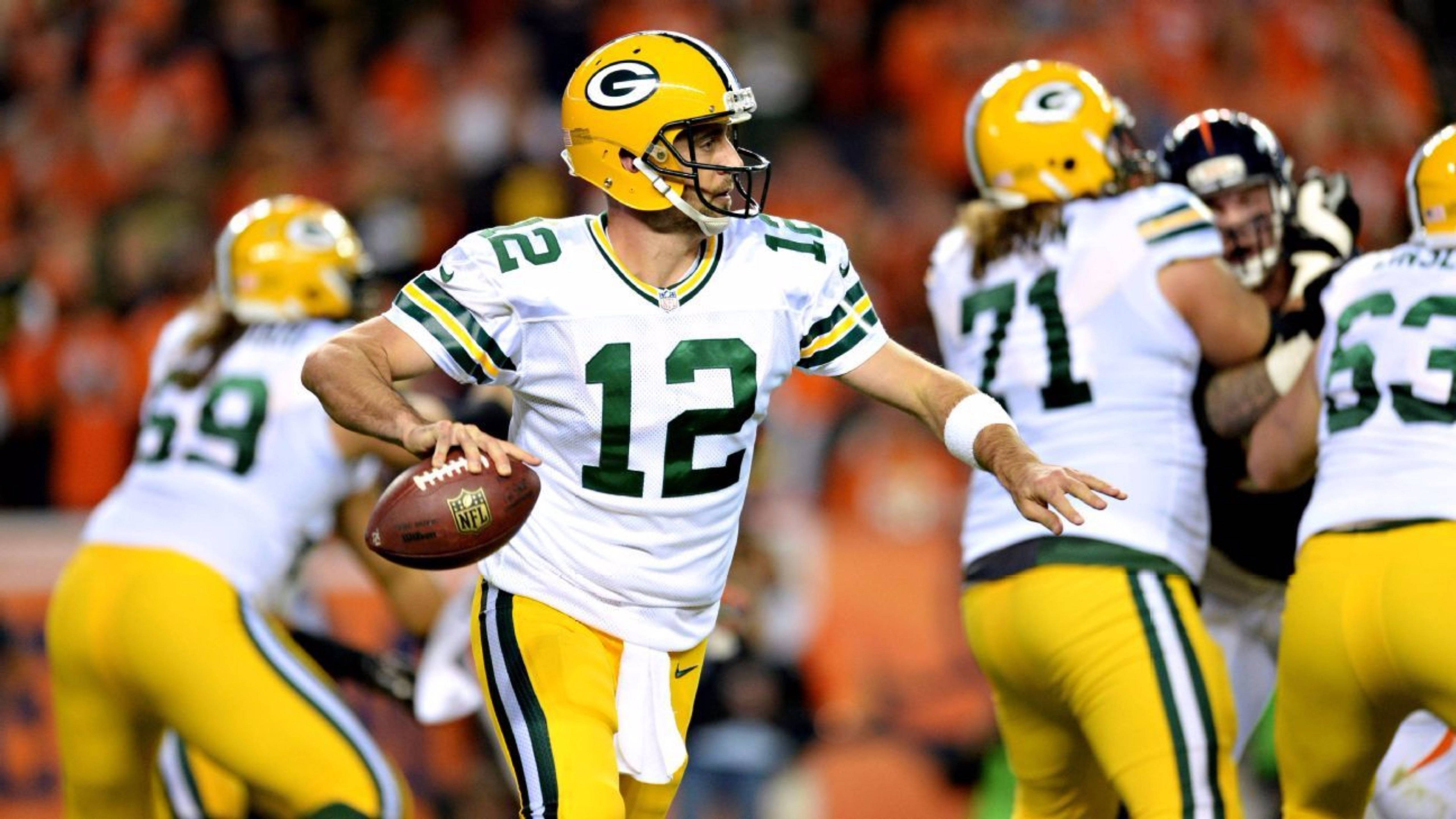 阿隆·羅傑斯 包裝工隊 NFL球隊 壁紙 — 綠灣包裝工隊的四分衛身穿白色和黃色球衣，在夜間比賽中準備傳球。