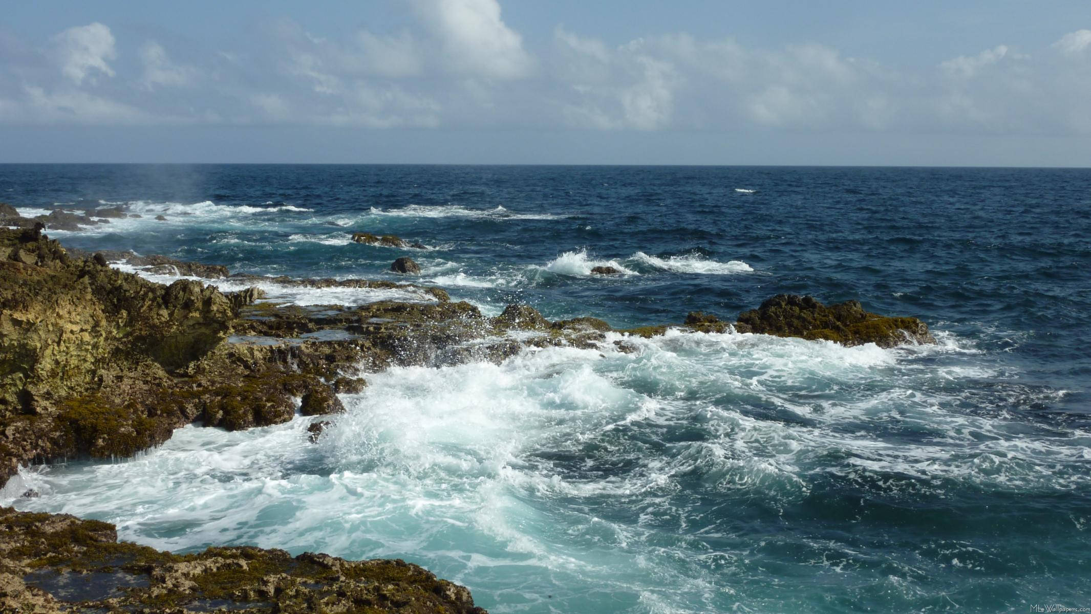 阿魯巴岩石海岸 壁紙 — 強勁的海浪拍打著堅固、長滿青苔的海岸岩石，天空部分多雲。