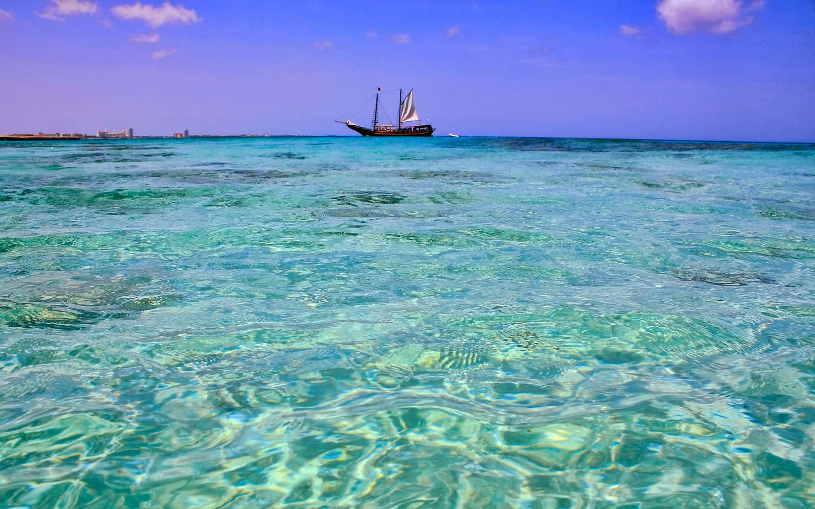 阿魯巴海灘帆船風景 壁紙 — 一艘傳統帆船在清澈碧綠的海水上滑行，天空湛藍，白雲點綴。